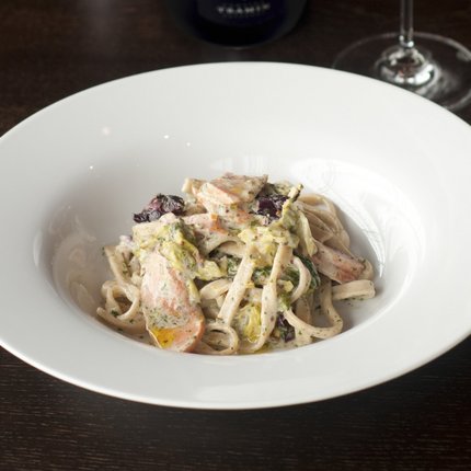 Pasta with creamy sauce served with a glass of white wine and a wine bottle