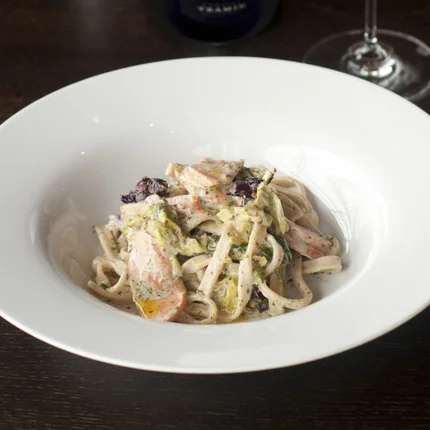 Pasta met romige saus geserveerd met een glas witte wijn en een fles wijn