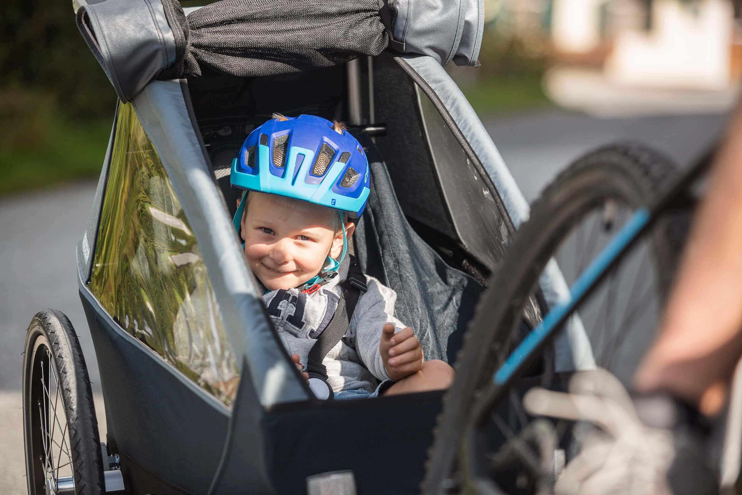 Kind mit Helm sitzt lächelnd in Fahrradanhänger