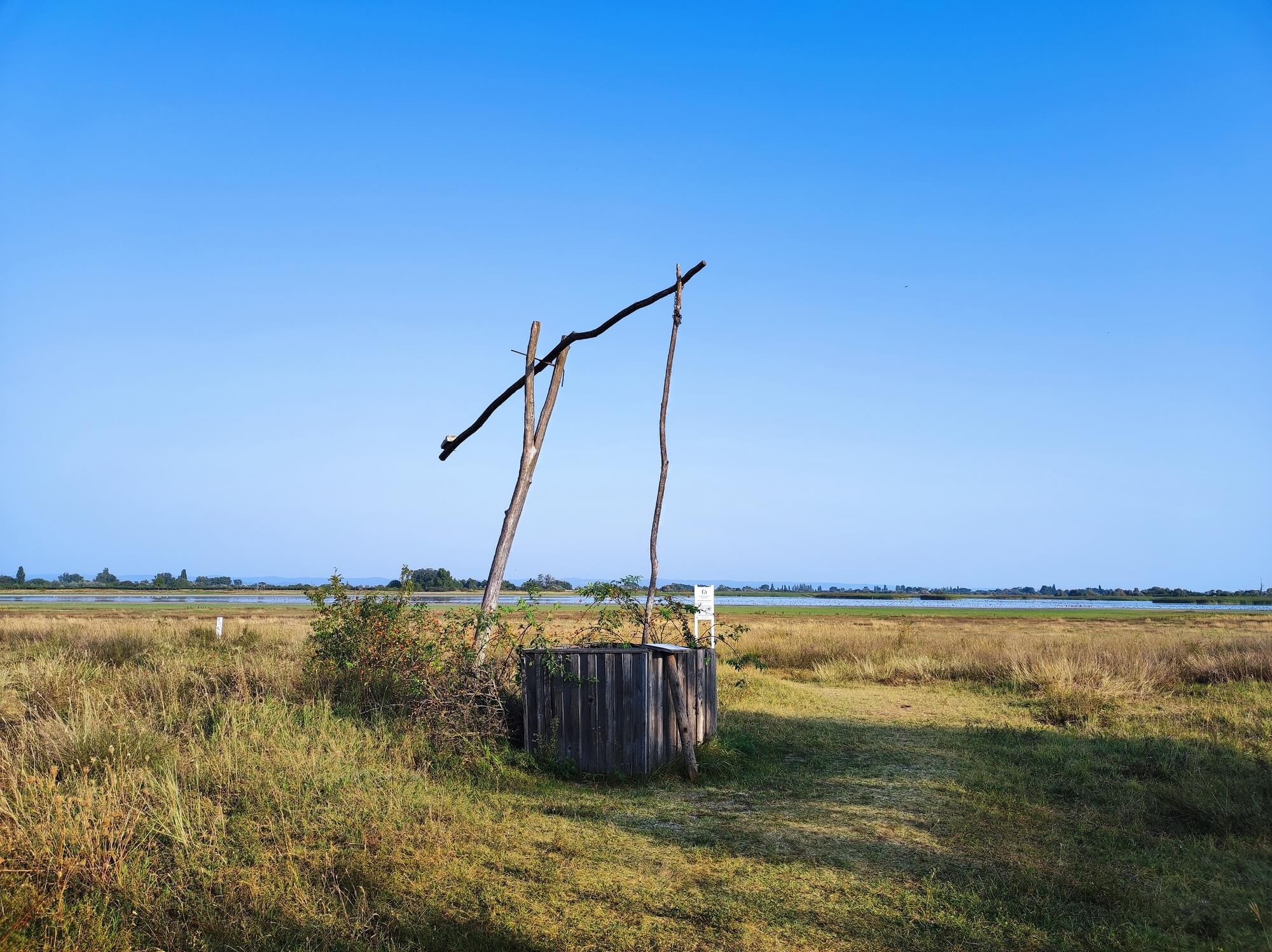 Holzbrunnen in einer weiten Graslandschaft unter klarem blauem Himmel