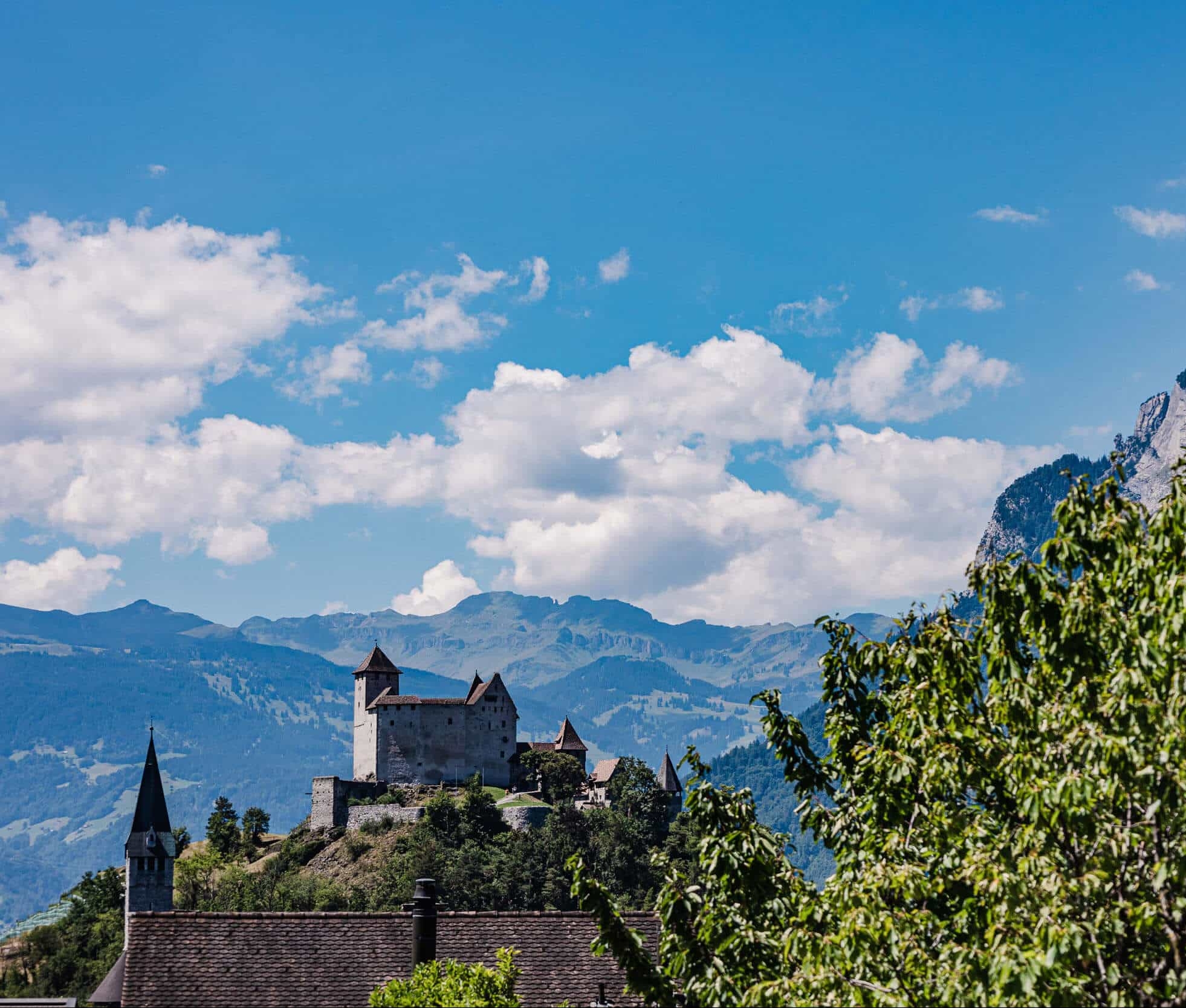 Burg auf einem Hügel vor Bergen und blauem Himmel mit Wolken