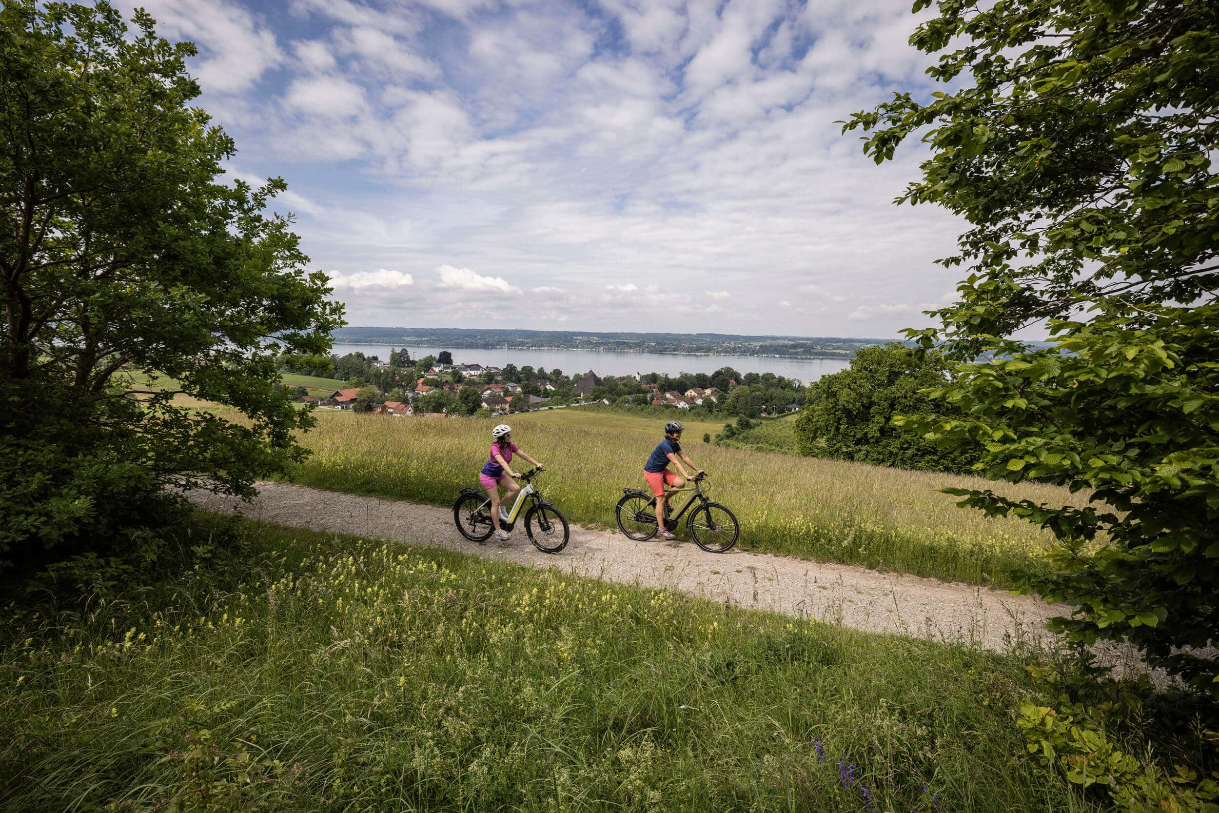 Zwei Personen fahren mit dem Fahrrad auf einem Weg mit Aussicht auf einen See
