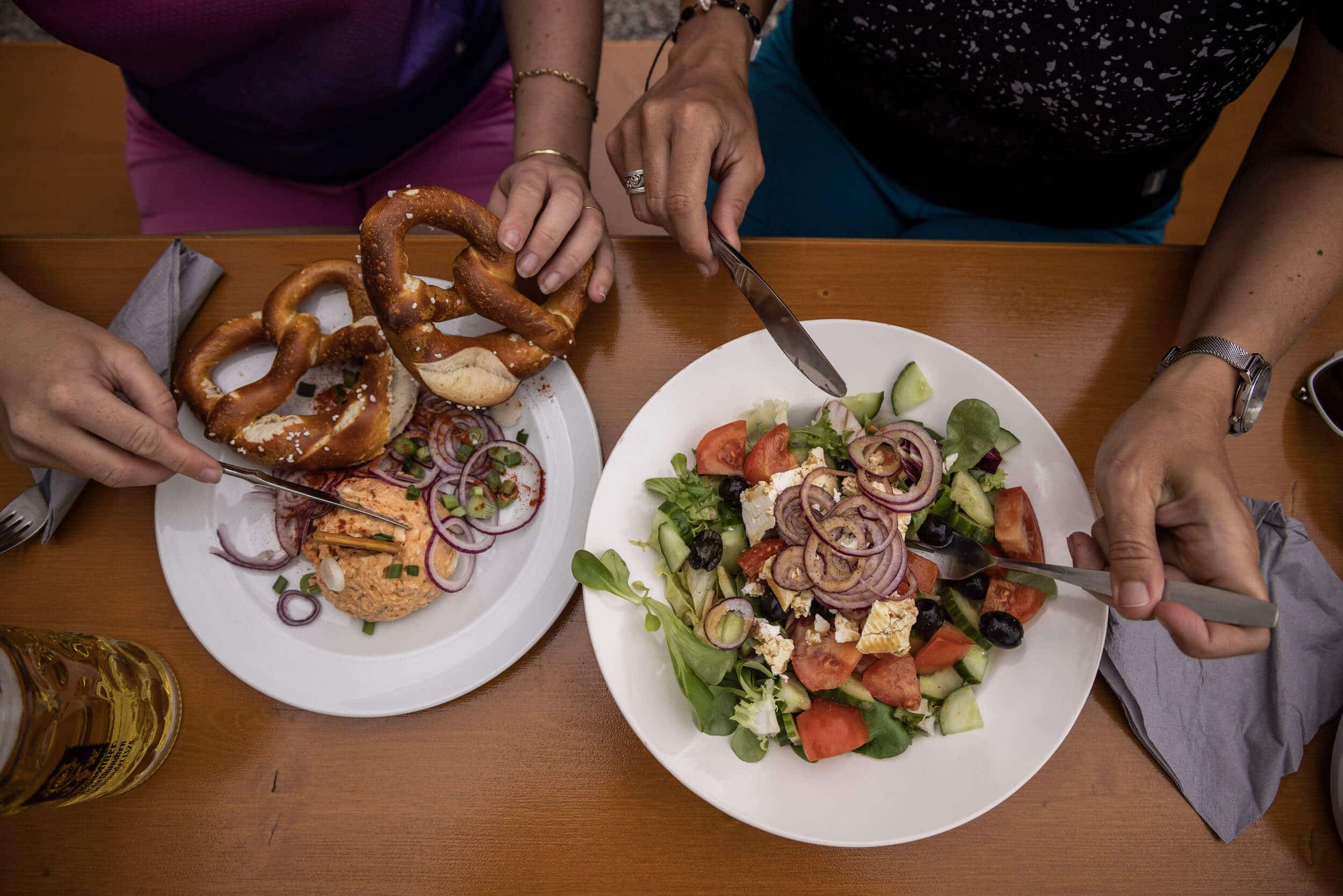 Zwei Personen essen Brezeln und Salat an einem Holztisch