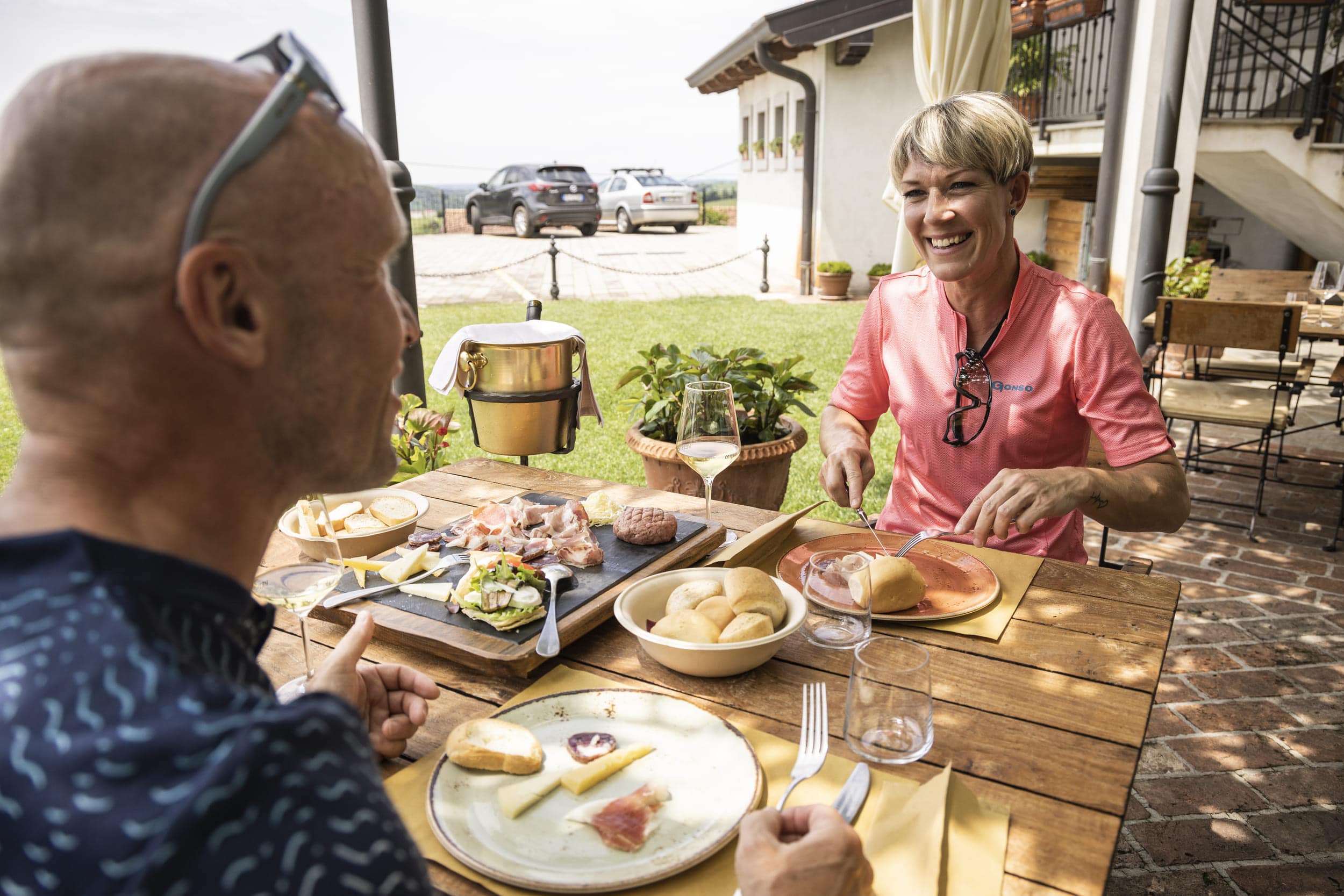 Zwei Menschen essen draußen an einem Holztisch mit Wein und Brot.
