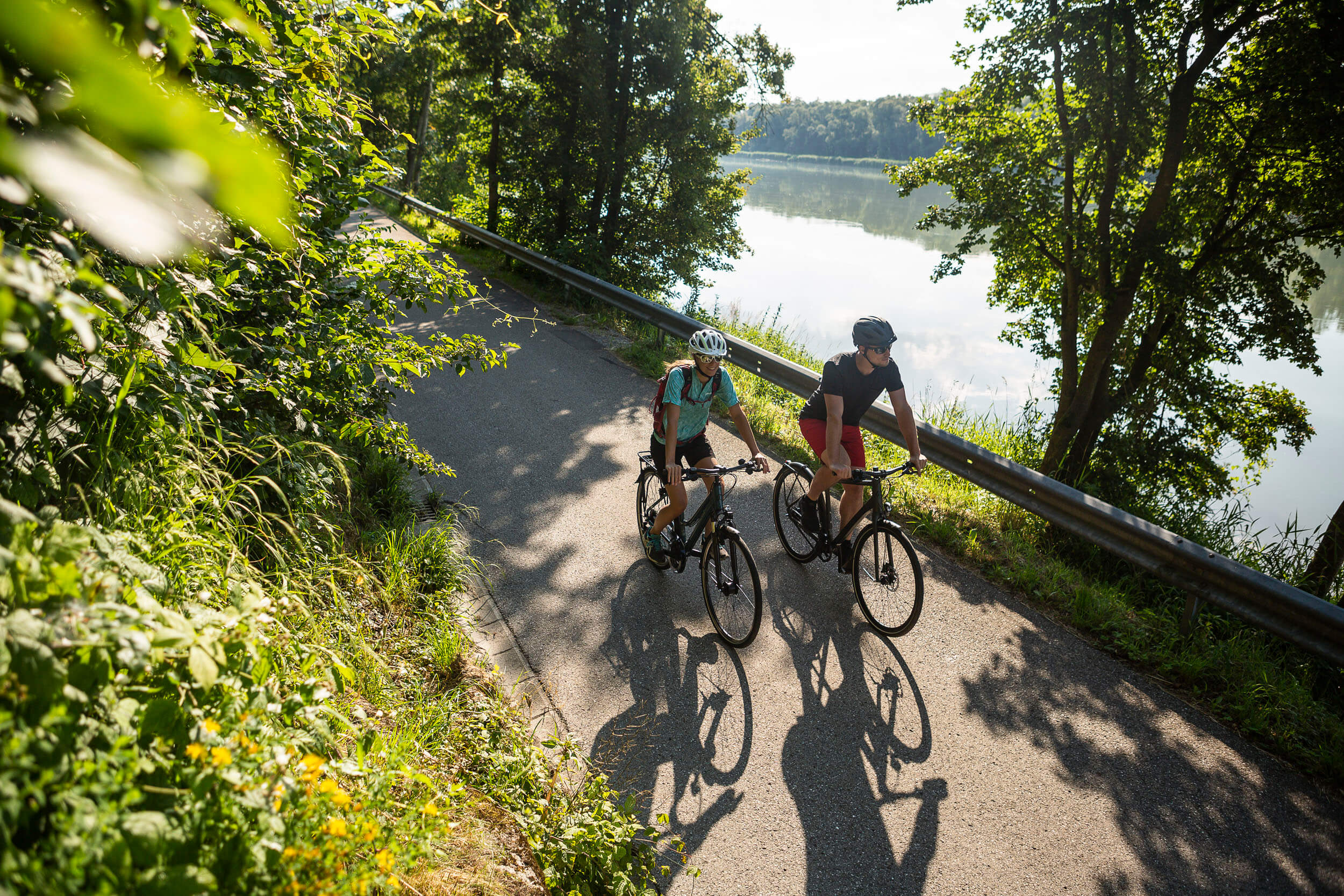 Zwei Radfahrer fahren auf einem Weg entlang eines Flusses bei Sonne