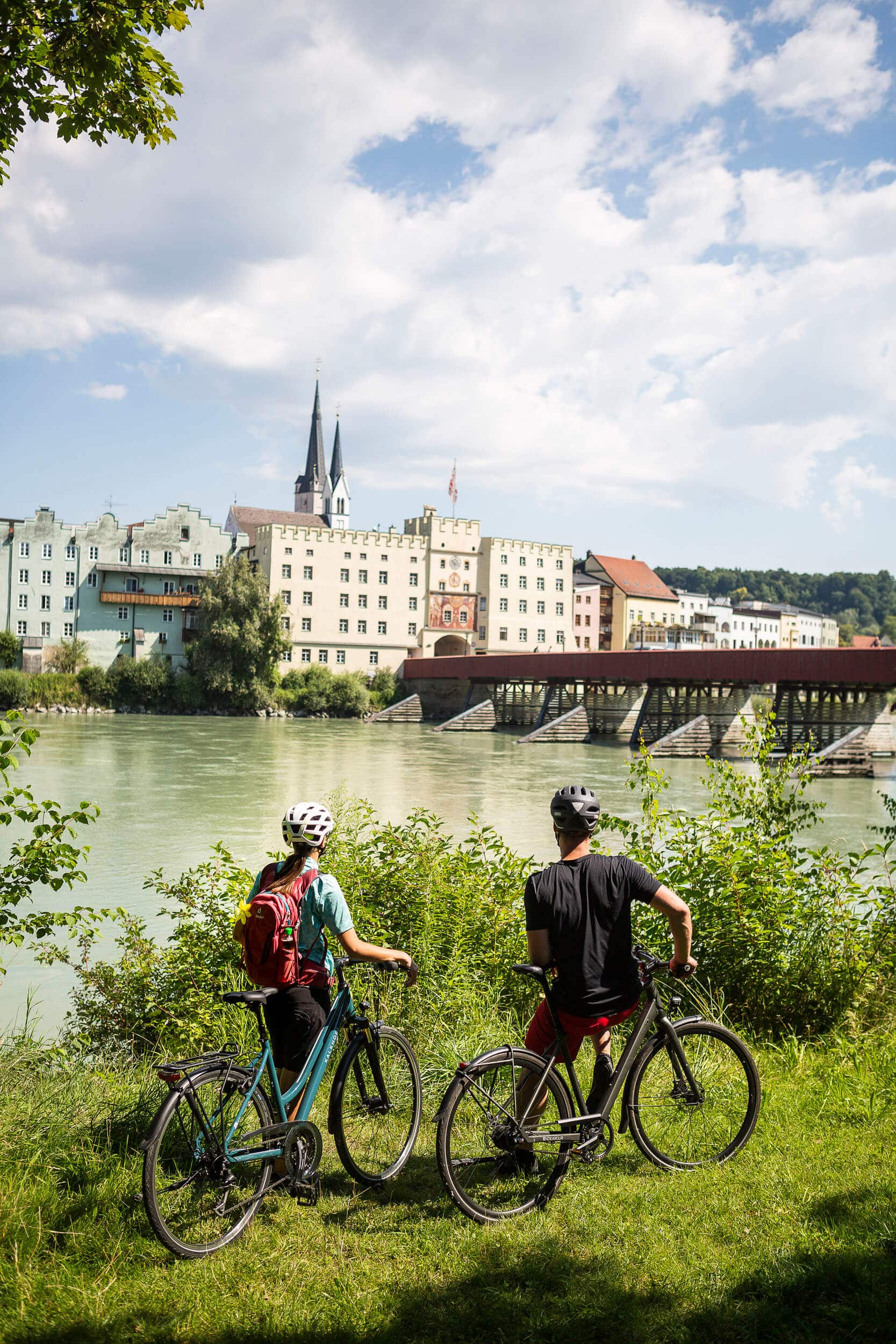Zwei Fahrradfahrer blicken auf eine Brücke über einen Fluss und historische Gebäude