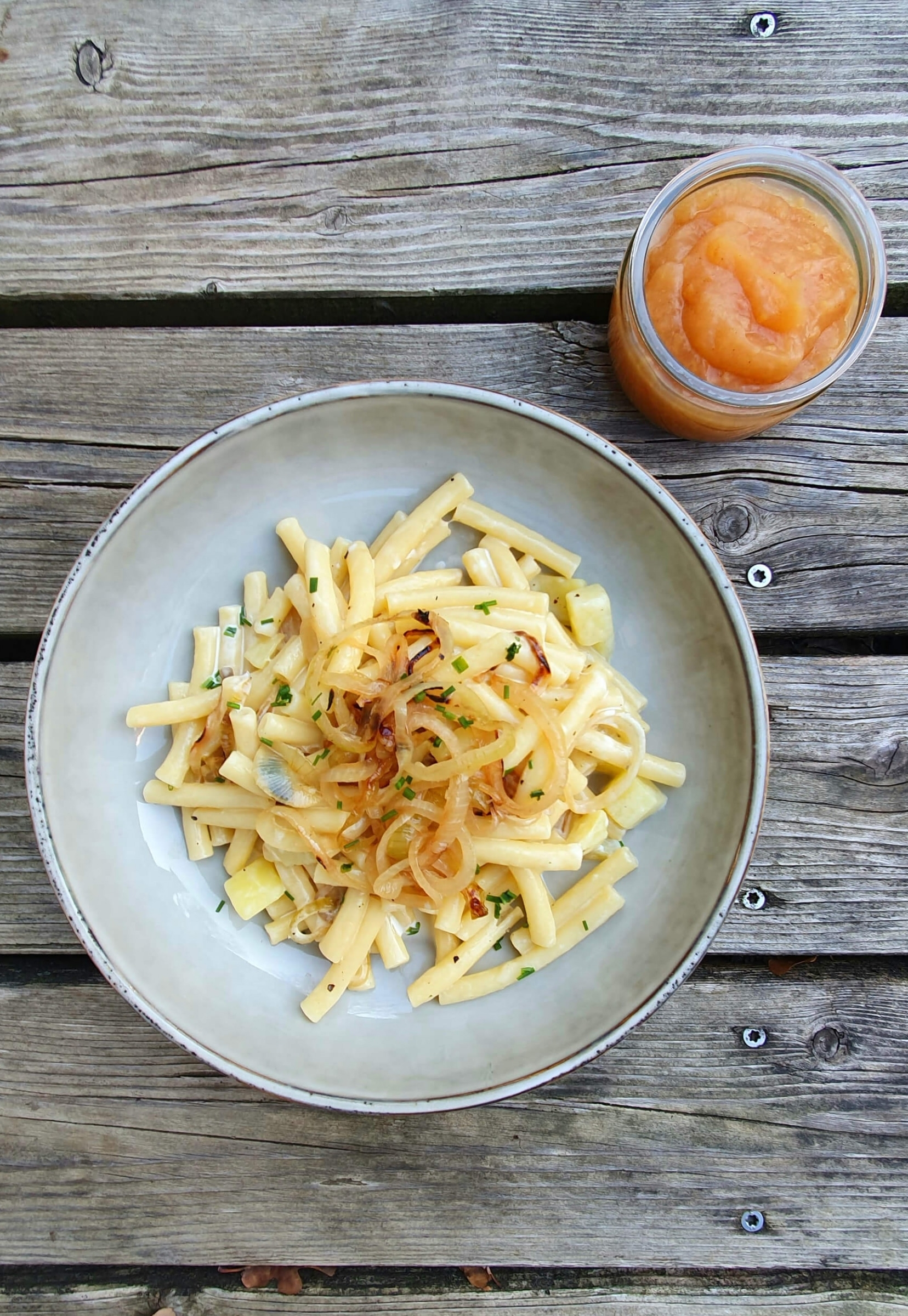 Plate of cheesy noodles with fried onions and apple sauce on wooden table
