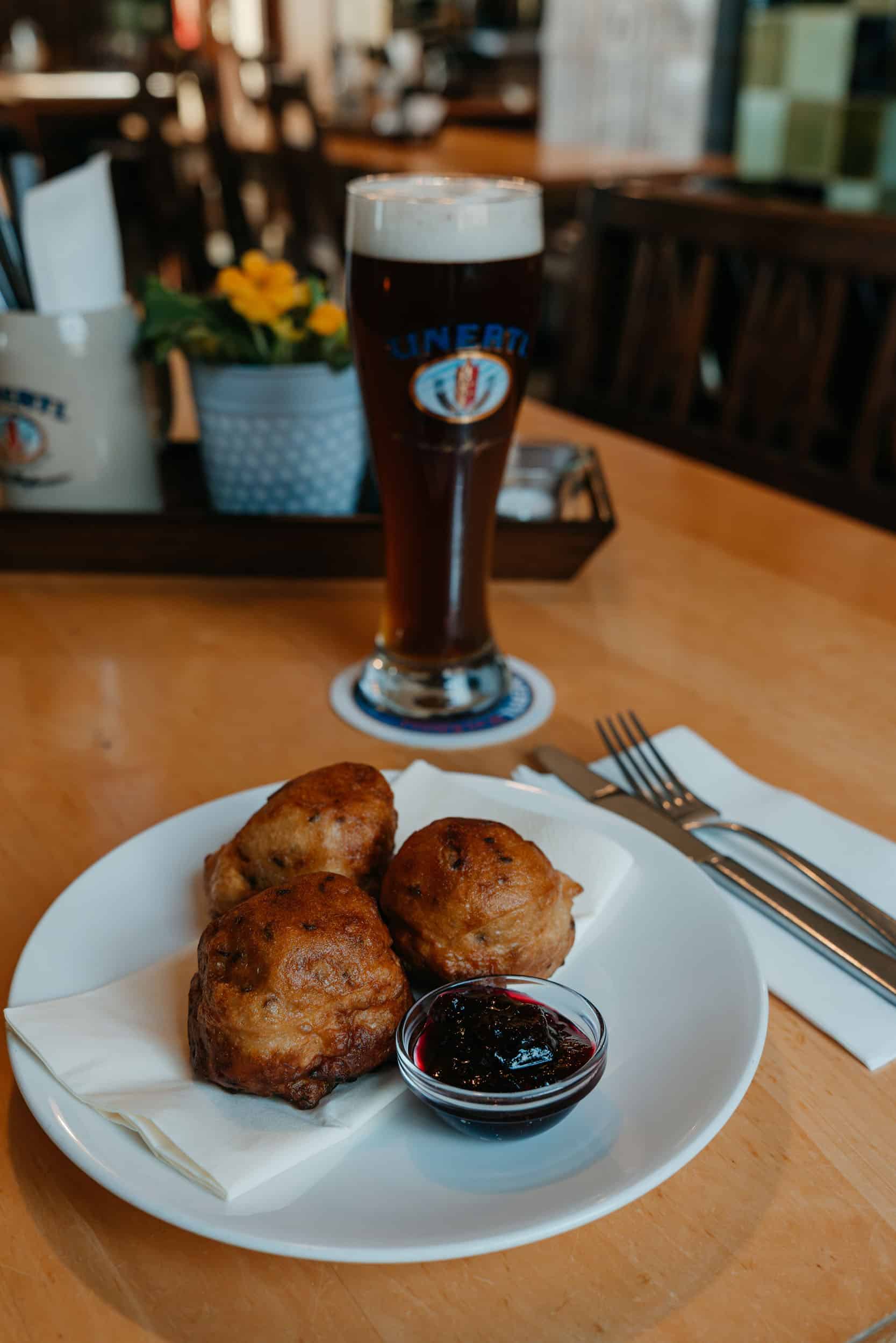 Three fried balls with red sauce and a glass of beer on the table