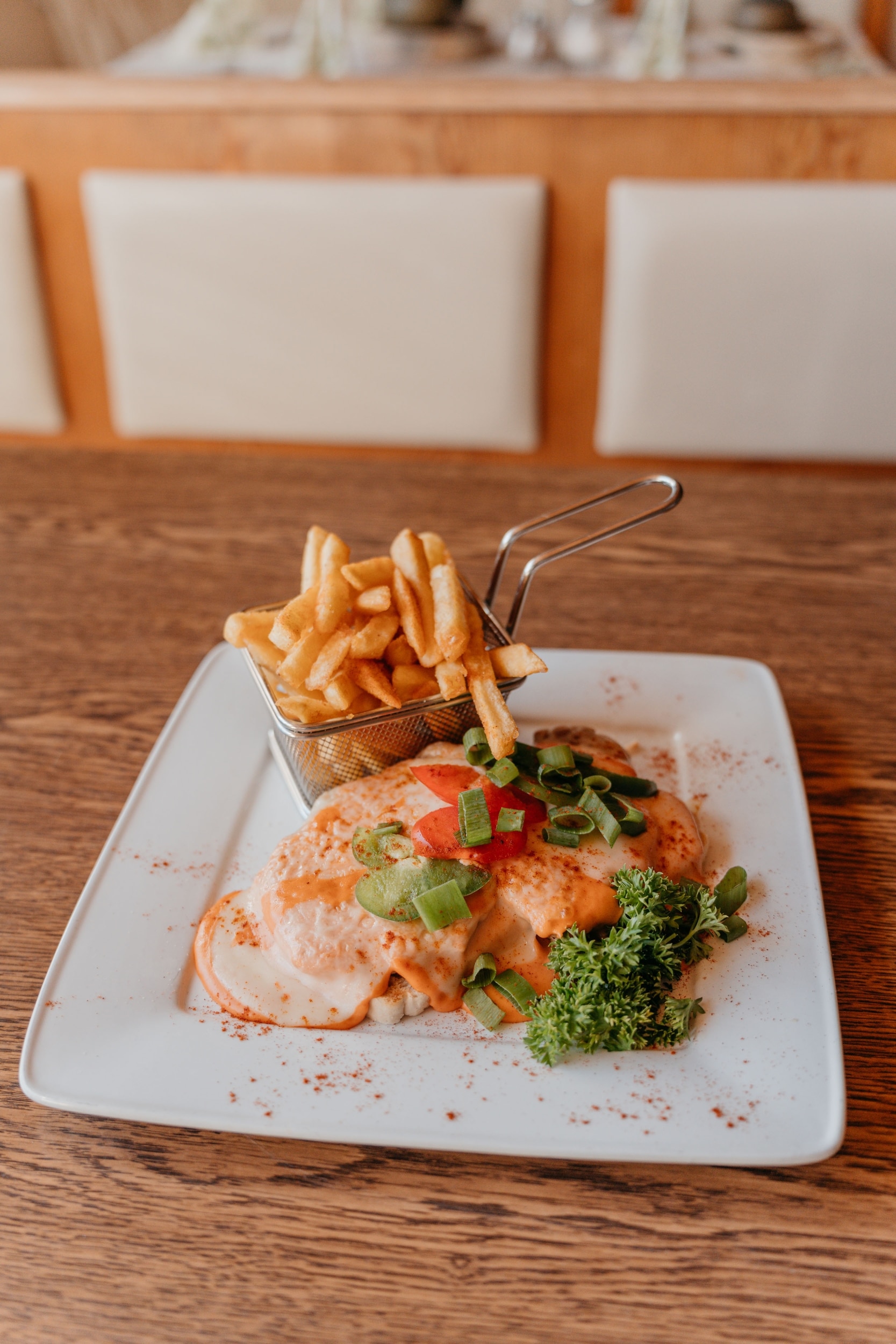 Schnitzel with cheese, vegetables and fries on white plate on wooden table