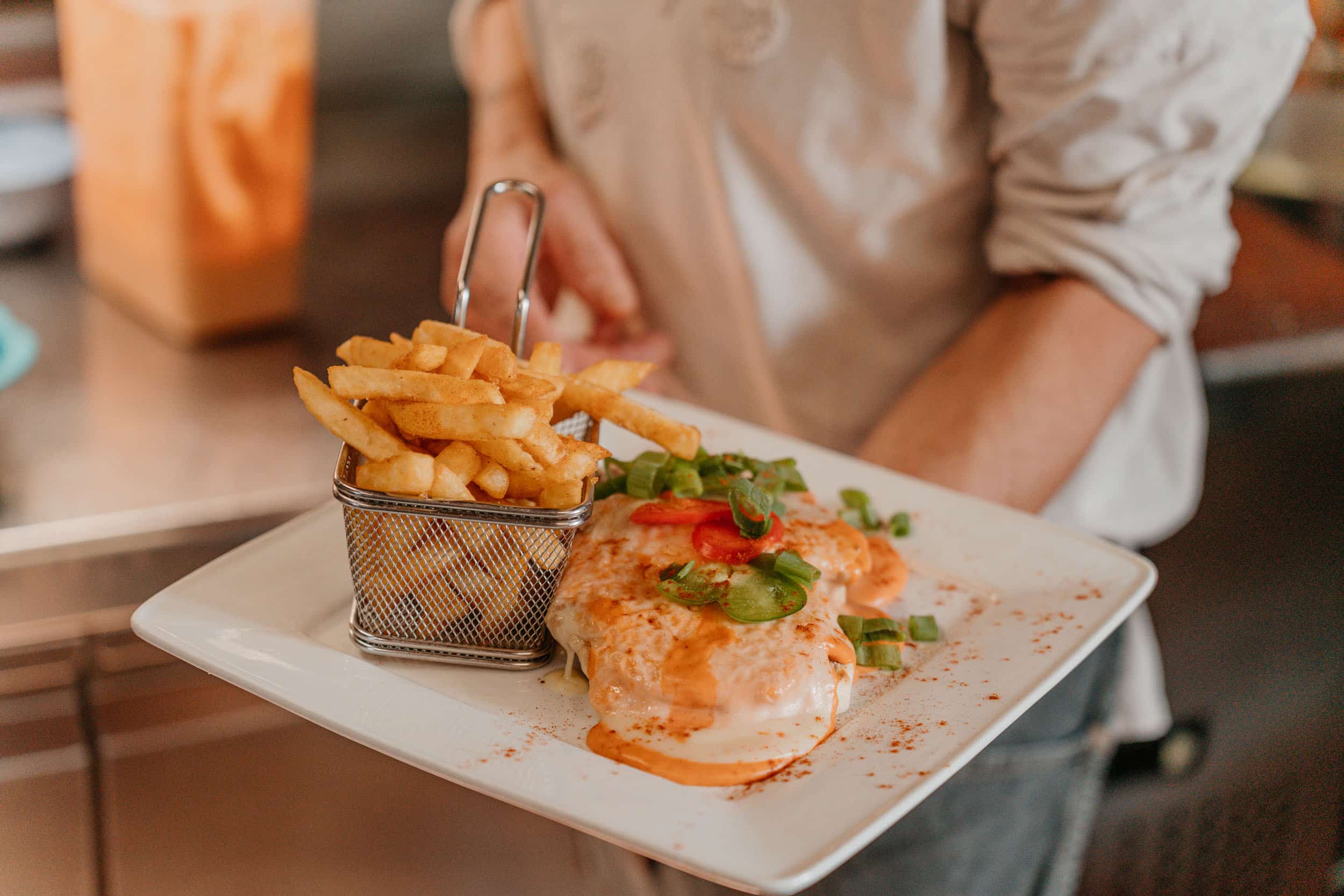 Person serving plate with fries and dish covered in sauce
