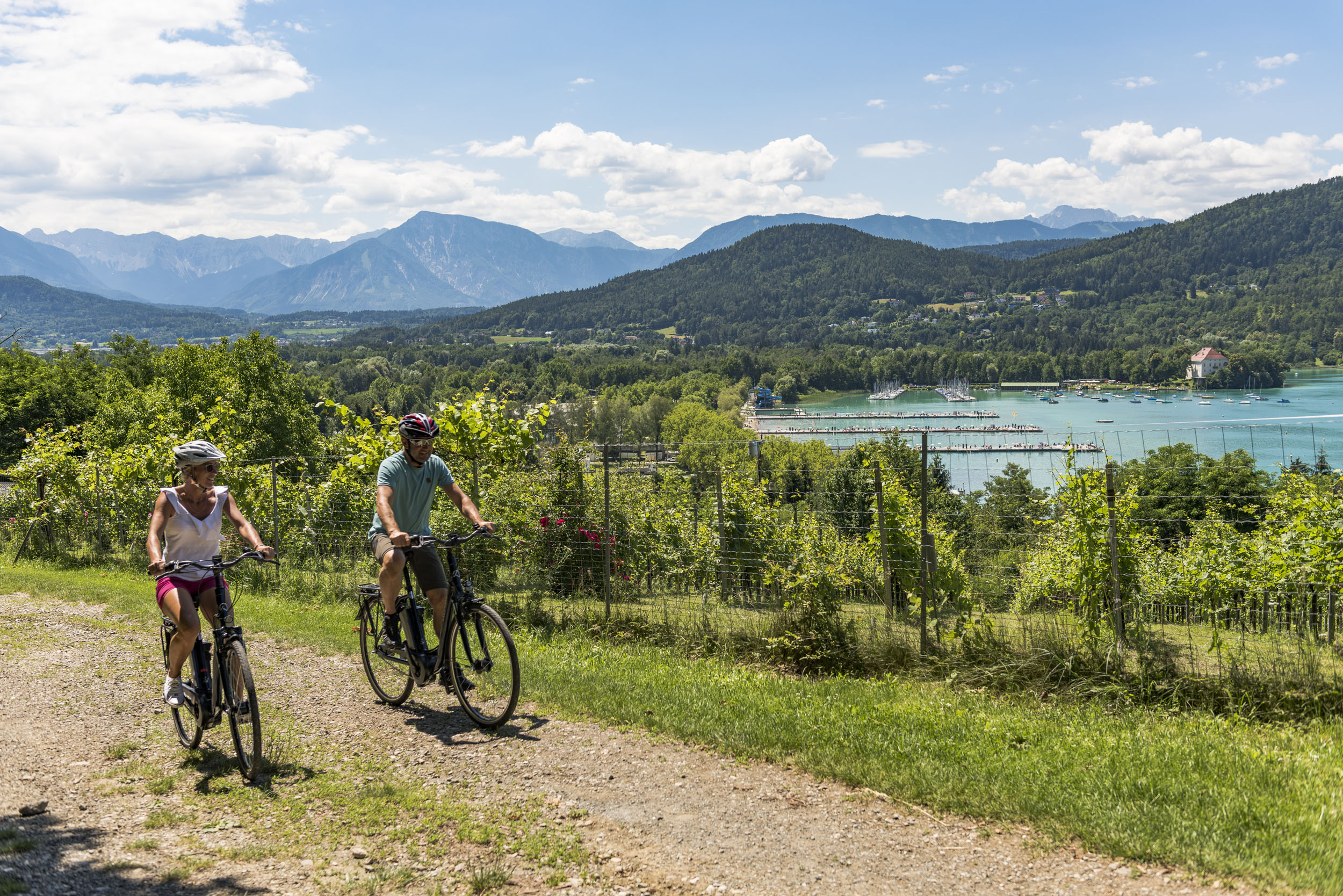 Zwei Radfahrer auf einem Weg mit Alpen und See im Hintergrund
