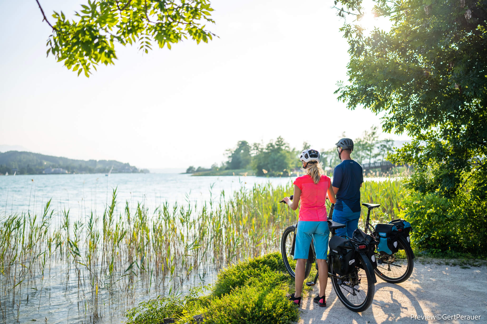 Paar mit Fahrrädern blickt auf einen sonnigen See am bewachsenen Ufer
