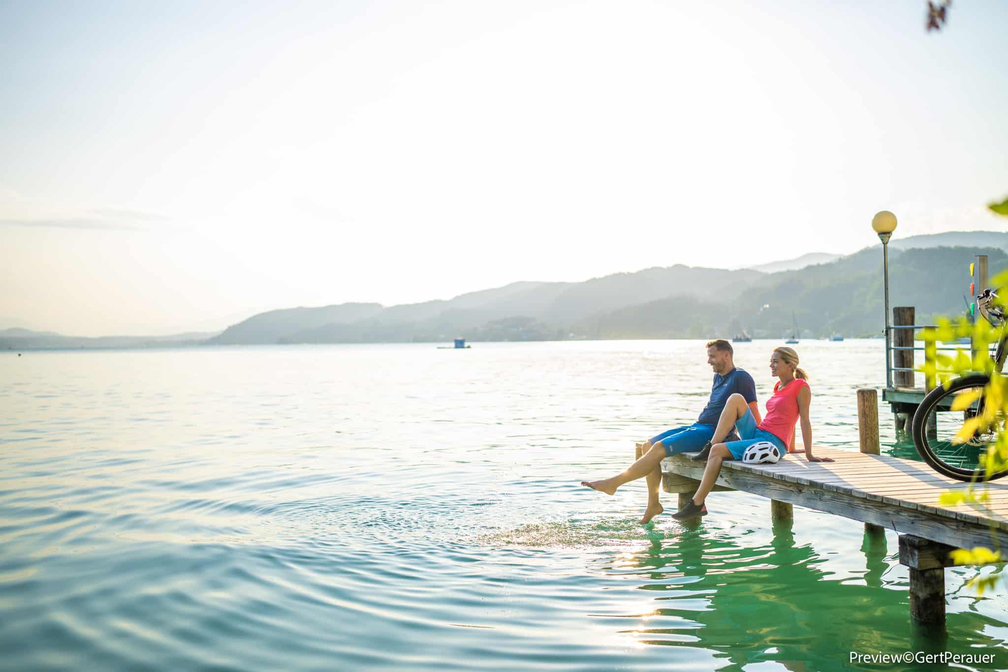 Paar sitzt auf Steg neben See, baumelt mit Füßen im Wasser
