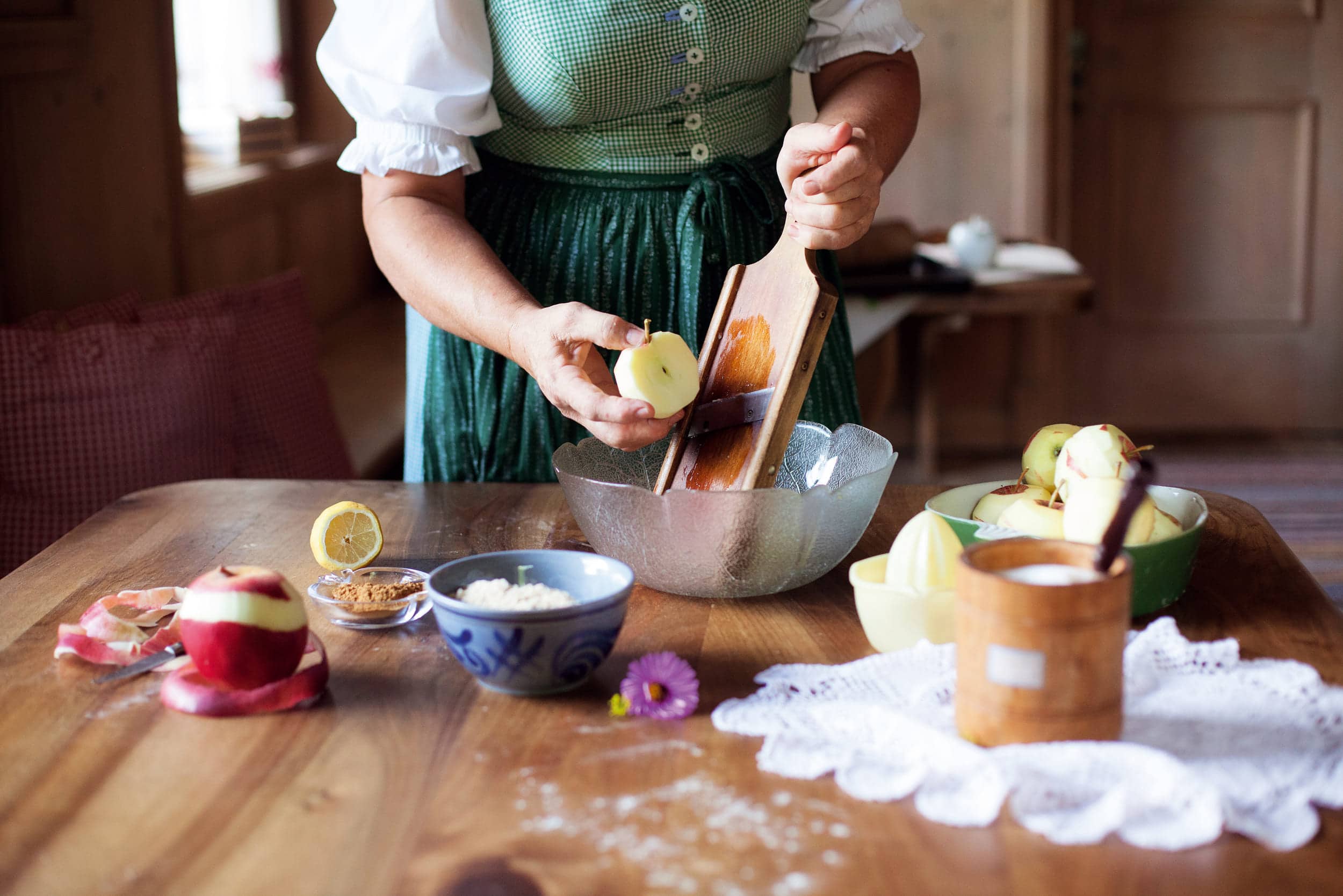 Person grating apple over glass bowl with ingredients on wooden table