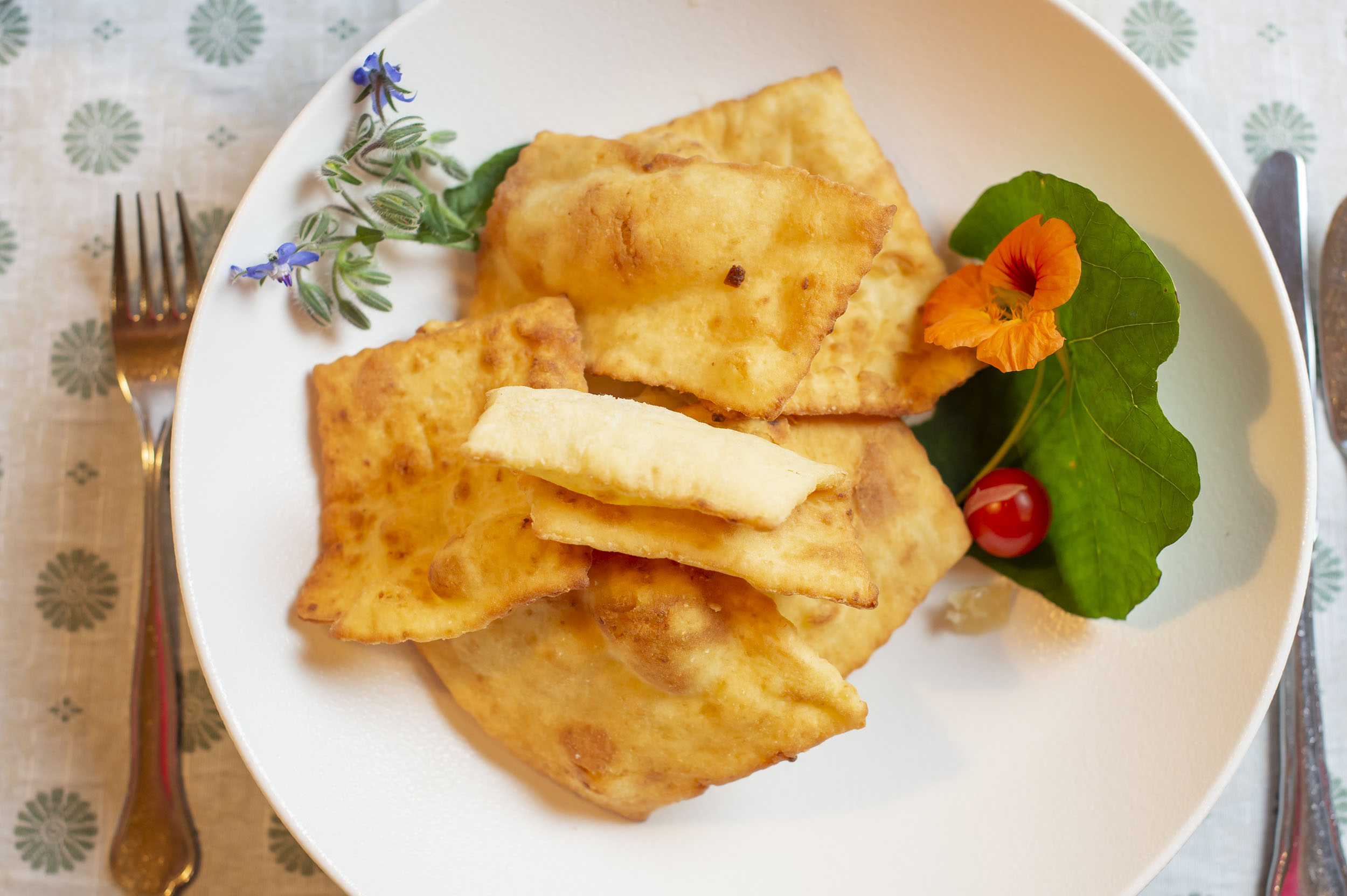 Fried dough pieces on white plate garnished with edible flower and herbs