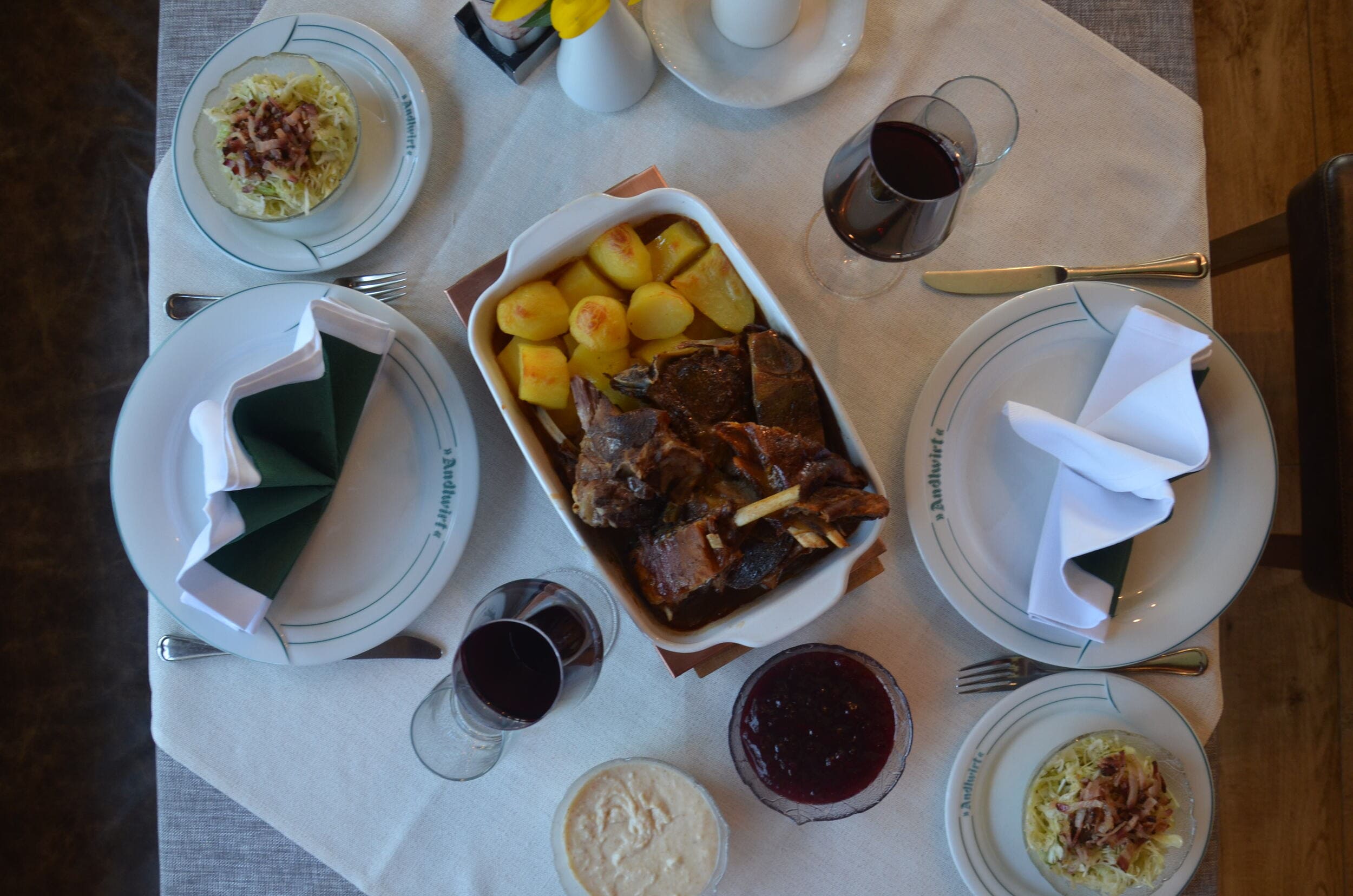 Table with roast meat, potatoes, salad, sauces, and red wine