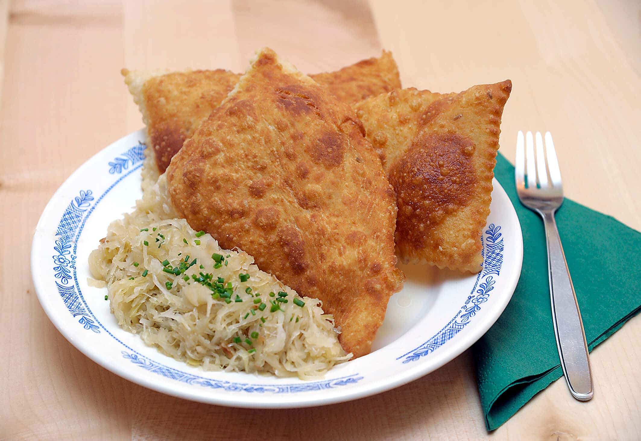 Plate with fried dumplings and sauerkraut beside fork on green napkin