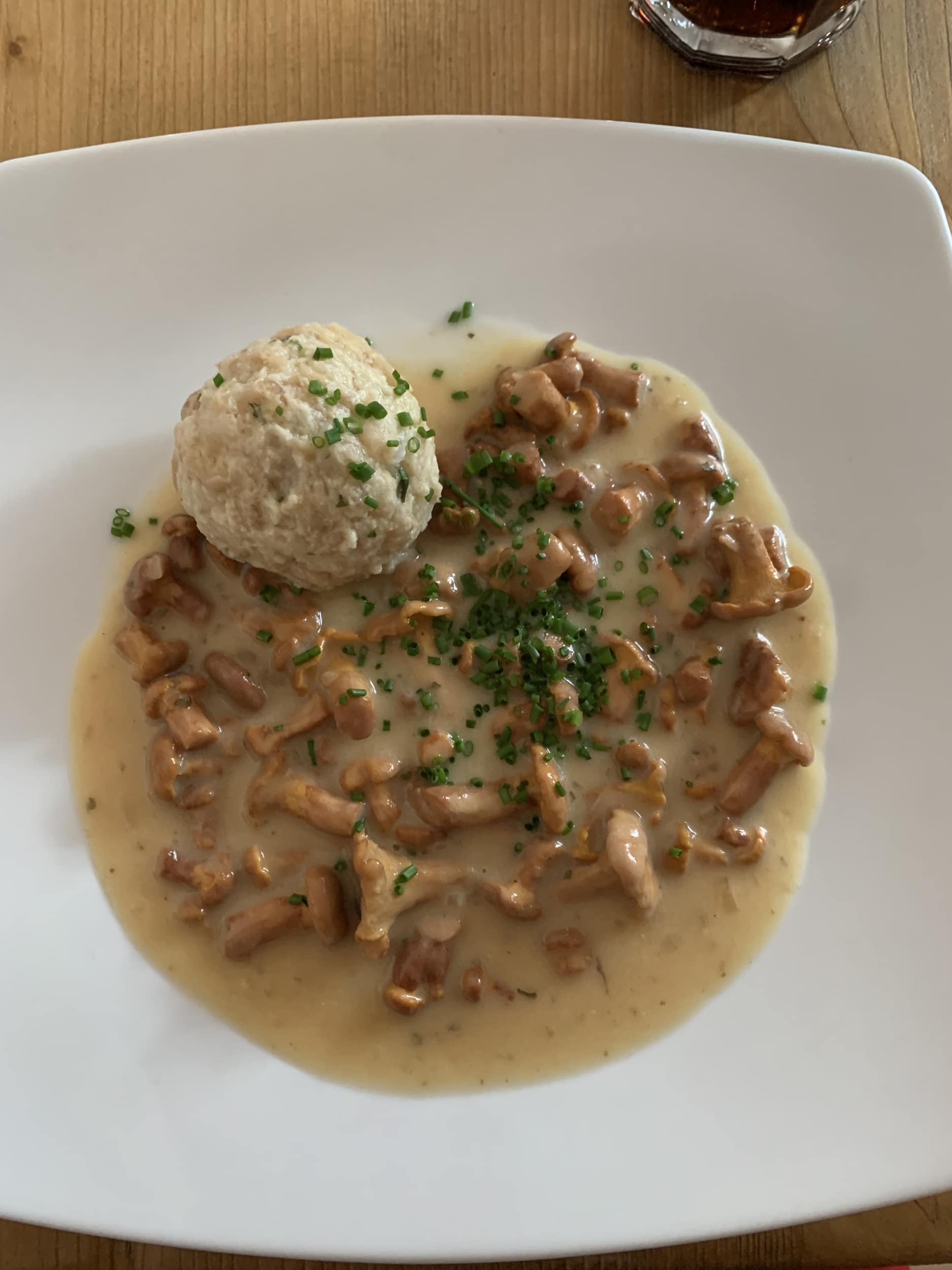 Bread dumpling with creamy chanterelles and chives on white plate