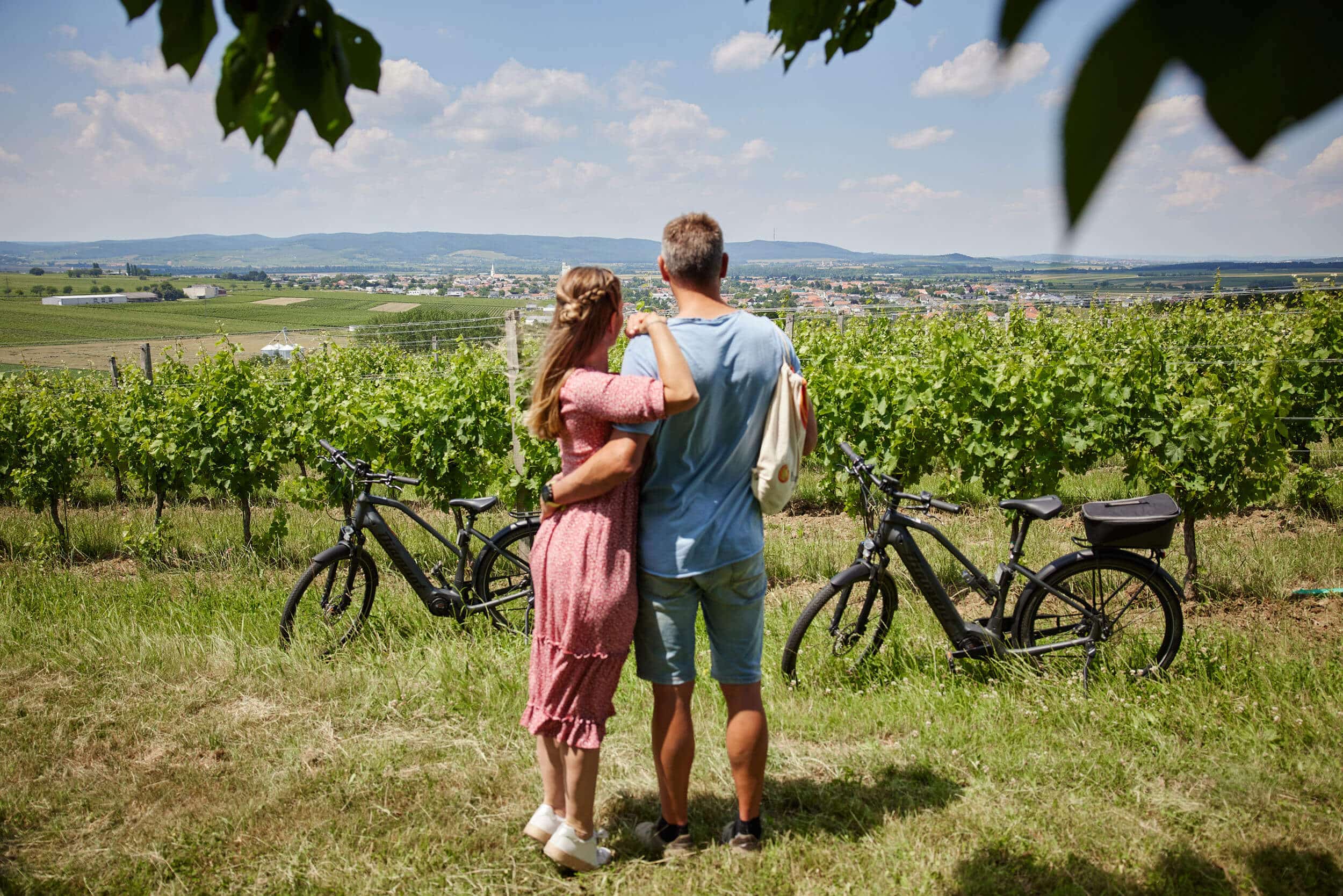 Paar mit Fahrrädern blickt auf Weinberg und Landschaft bei sonnigem Wetter