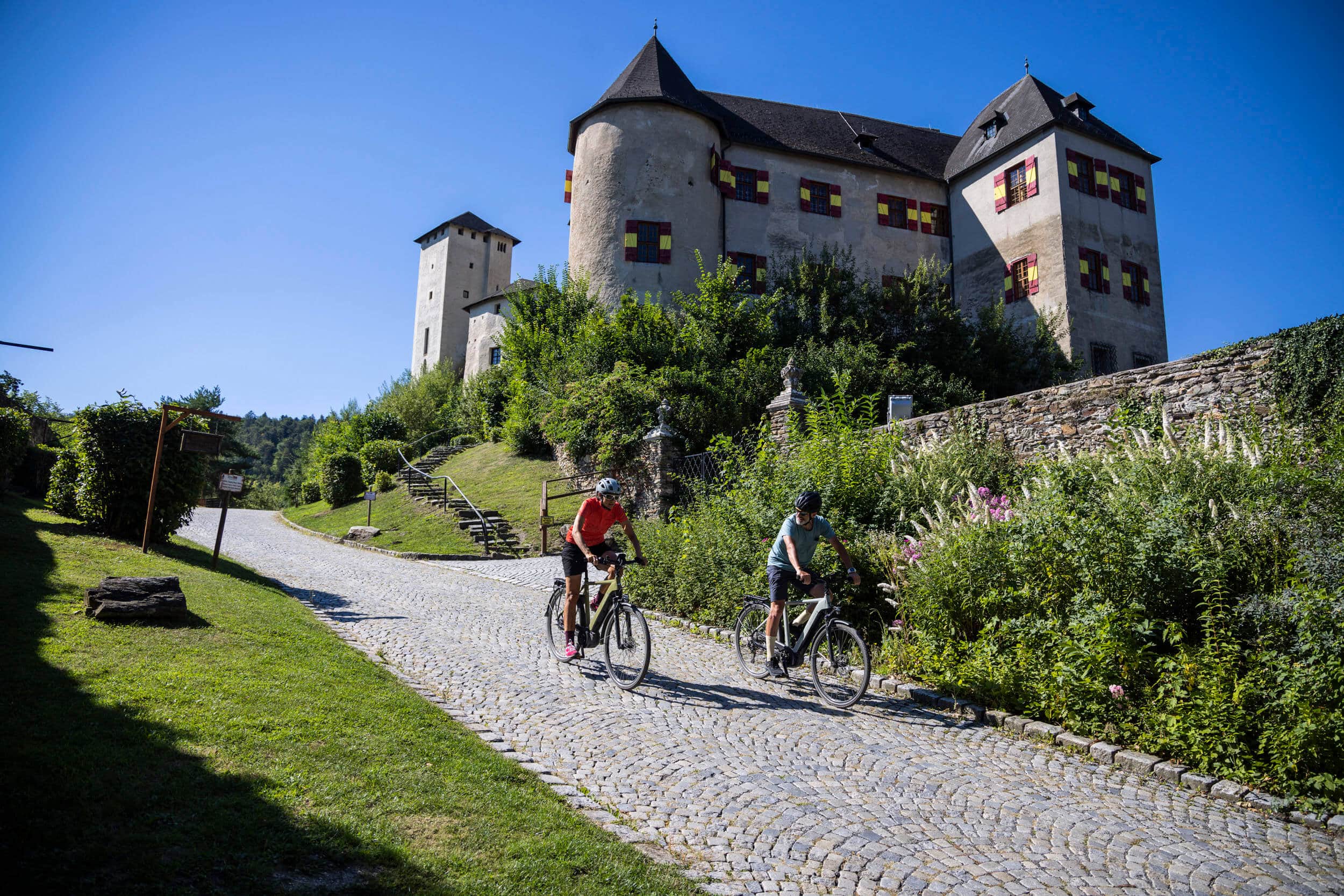 Two cyclists riding on cobblestone road with a historic castle in background