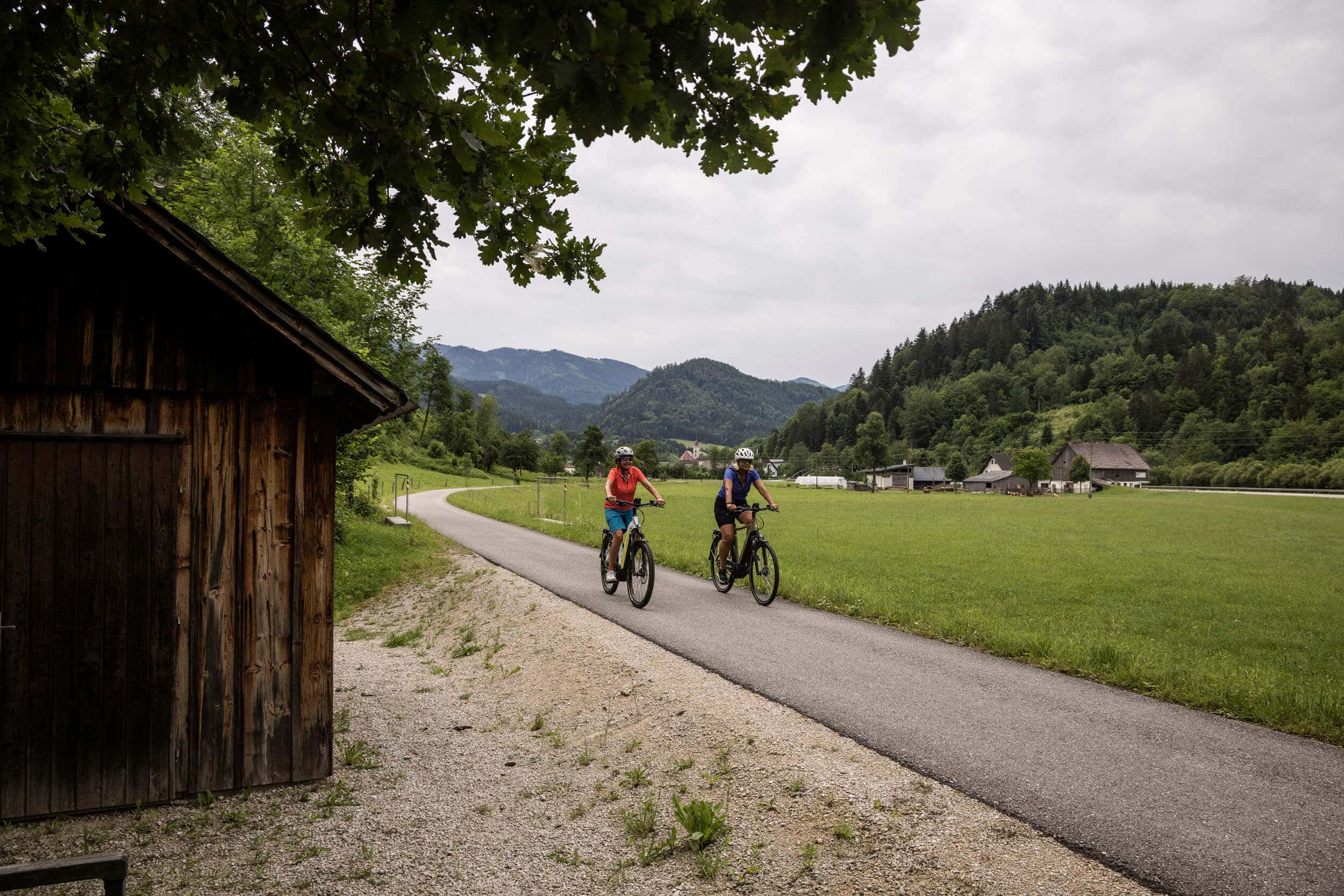 Zwei Radfahrer auf asphaltierter Straße in grüner Hügellandschaft