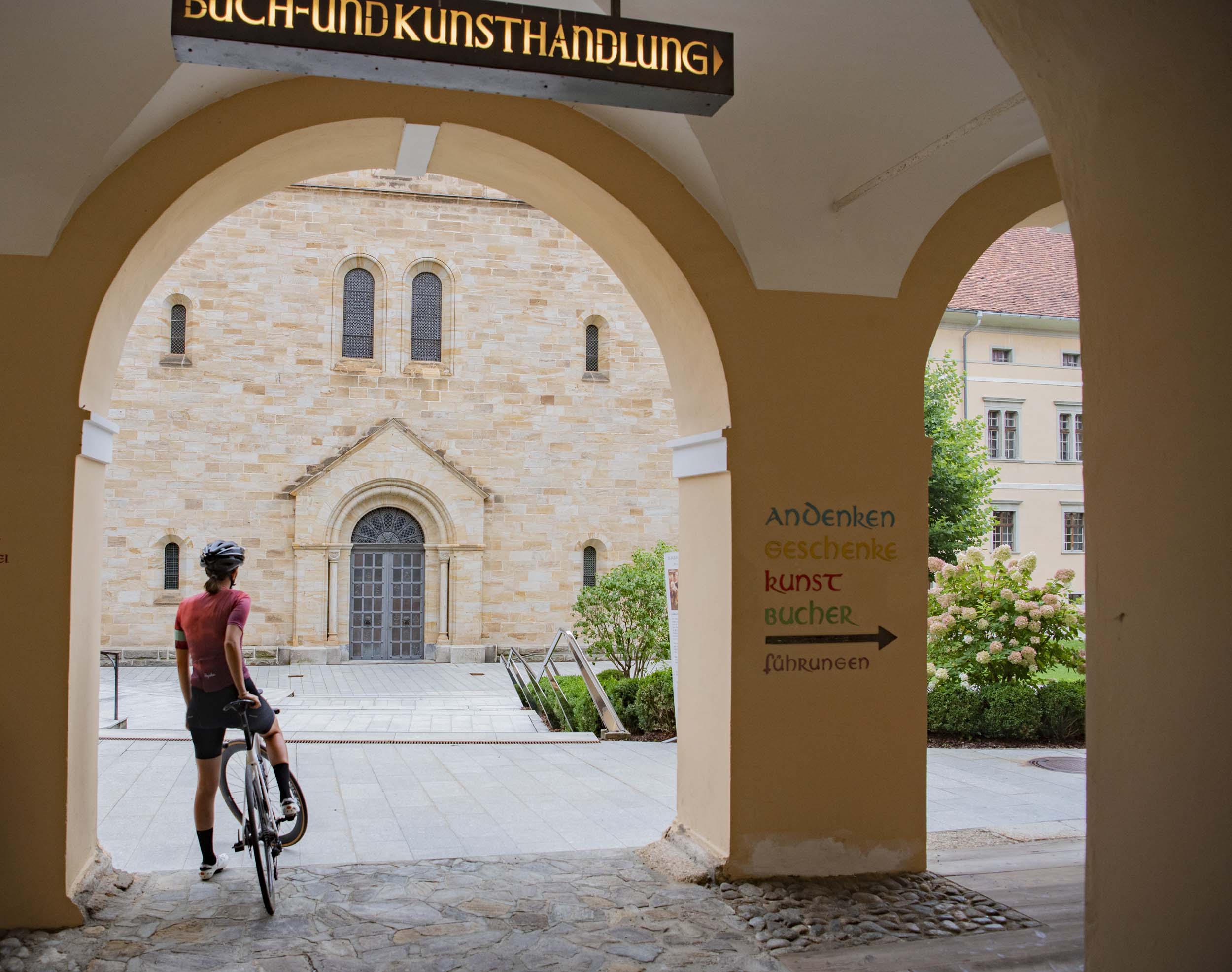 Person mit Fahrrad unter einem Torbogen vor einem historischen Gebäude