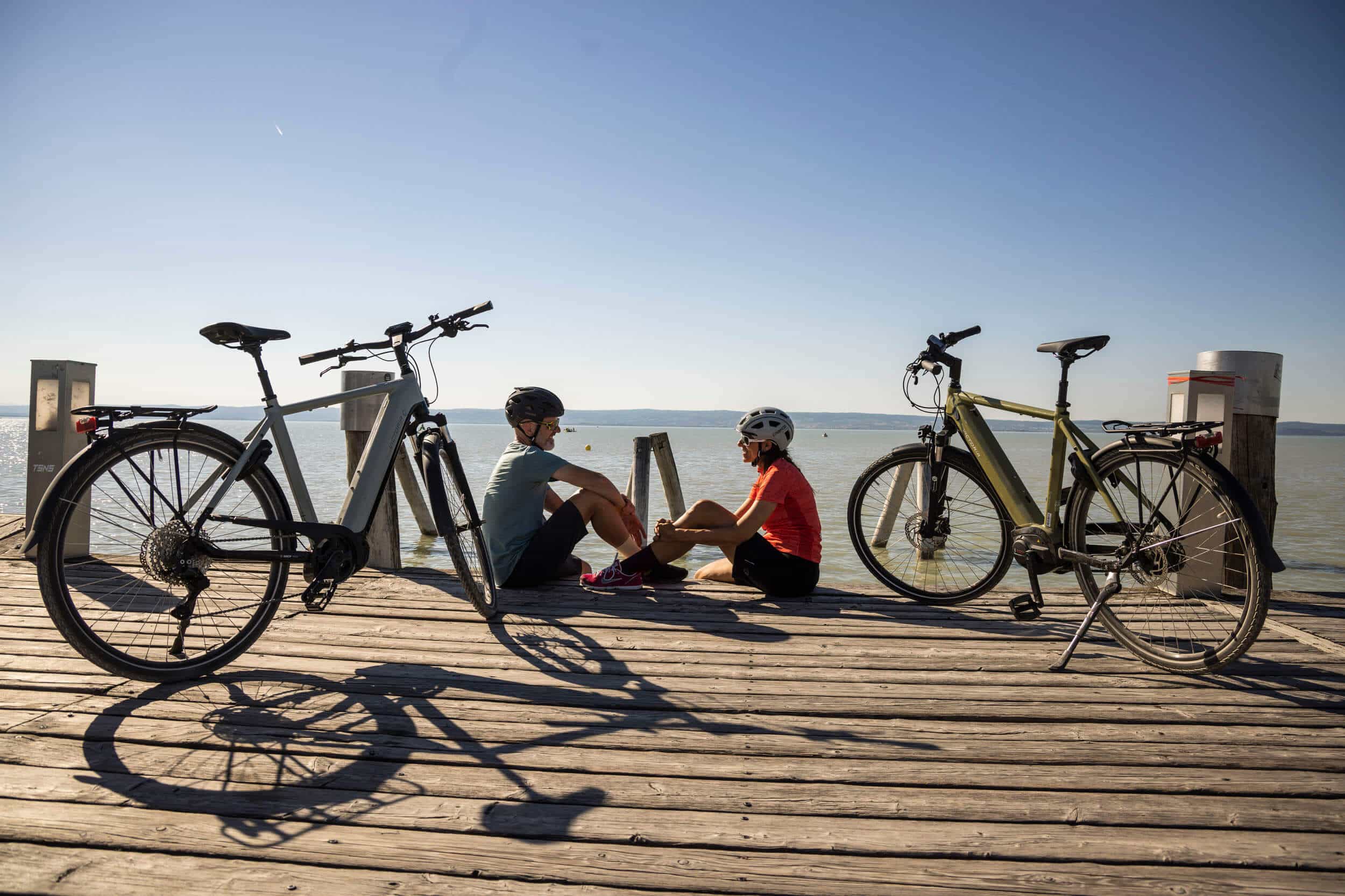 Zwei Radfahrer sitzen auf einem Steg am See mit ihren Fahrrädern daneben