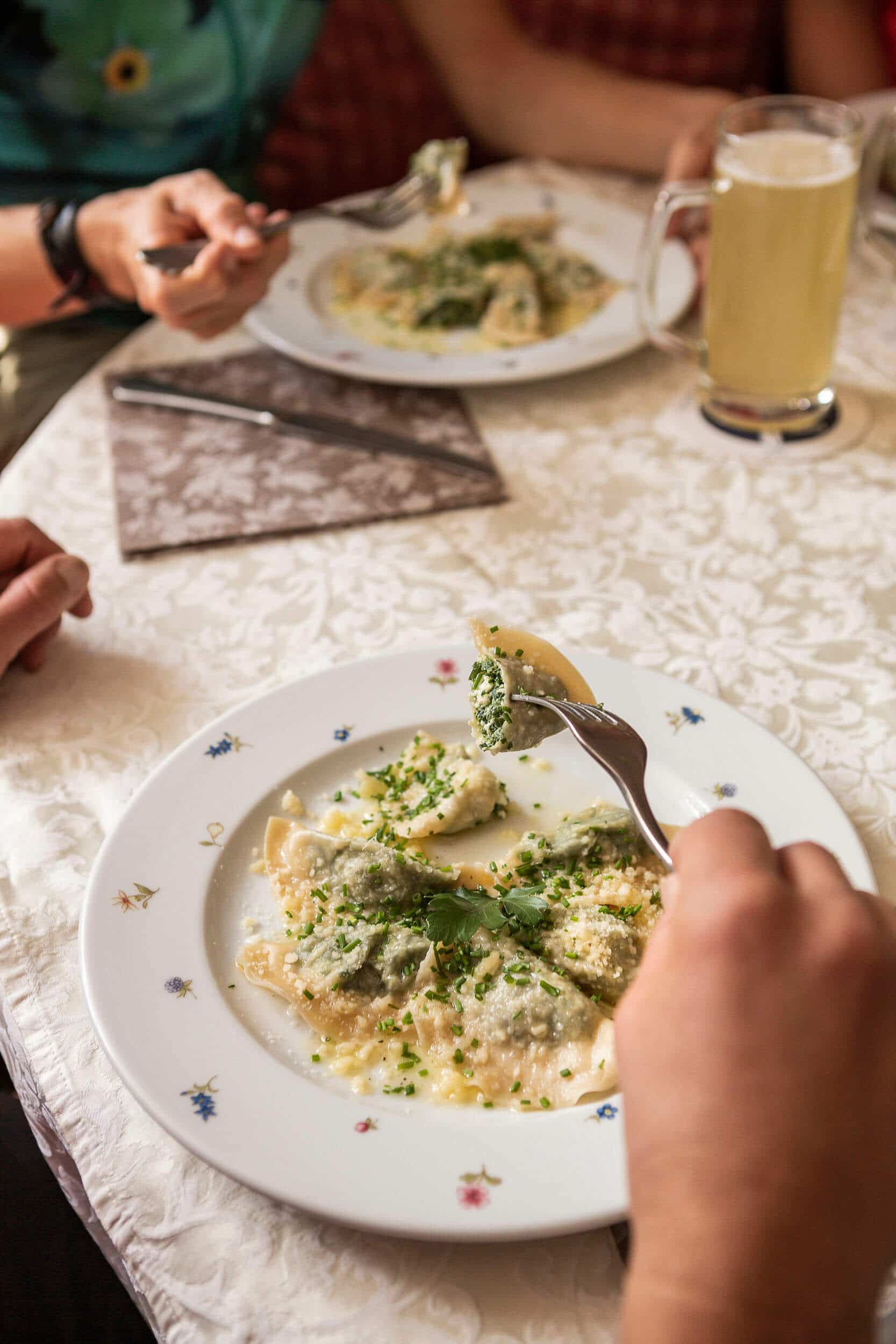 Person eating green filled ravioli with herbs at a set dining table