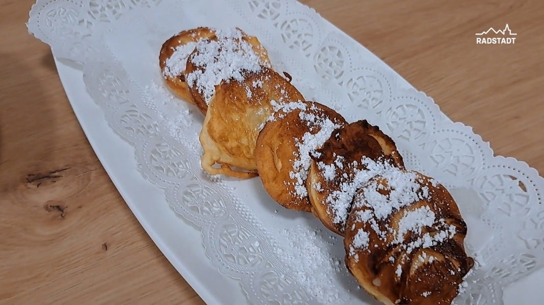Five fried apple slices with powdered sugar on a white plate