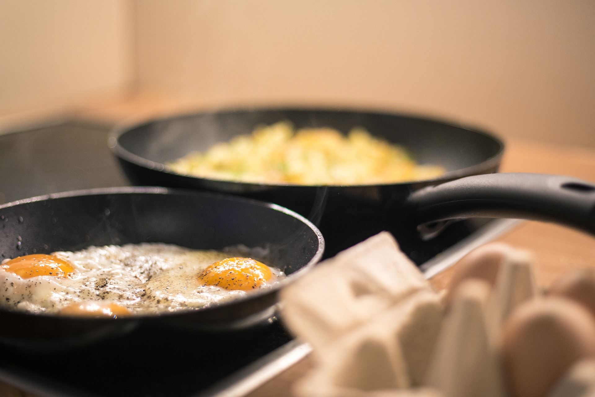 Fried eggs and a pan dish cooking on the stovetop in black pans