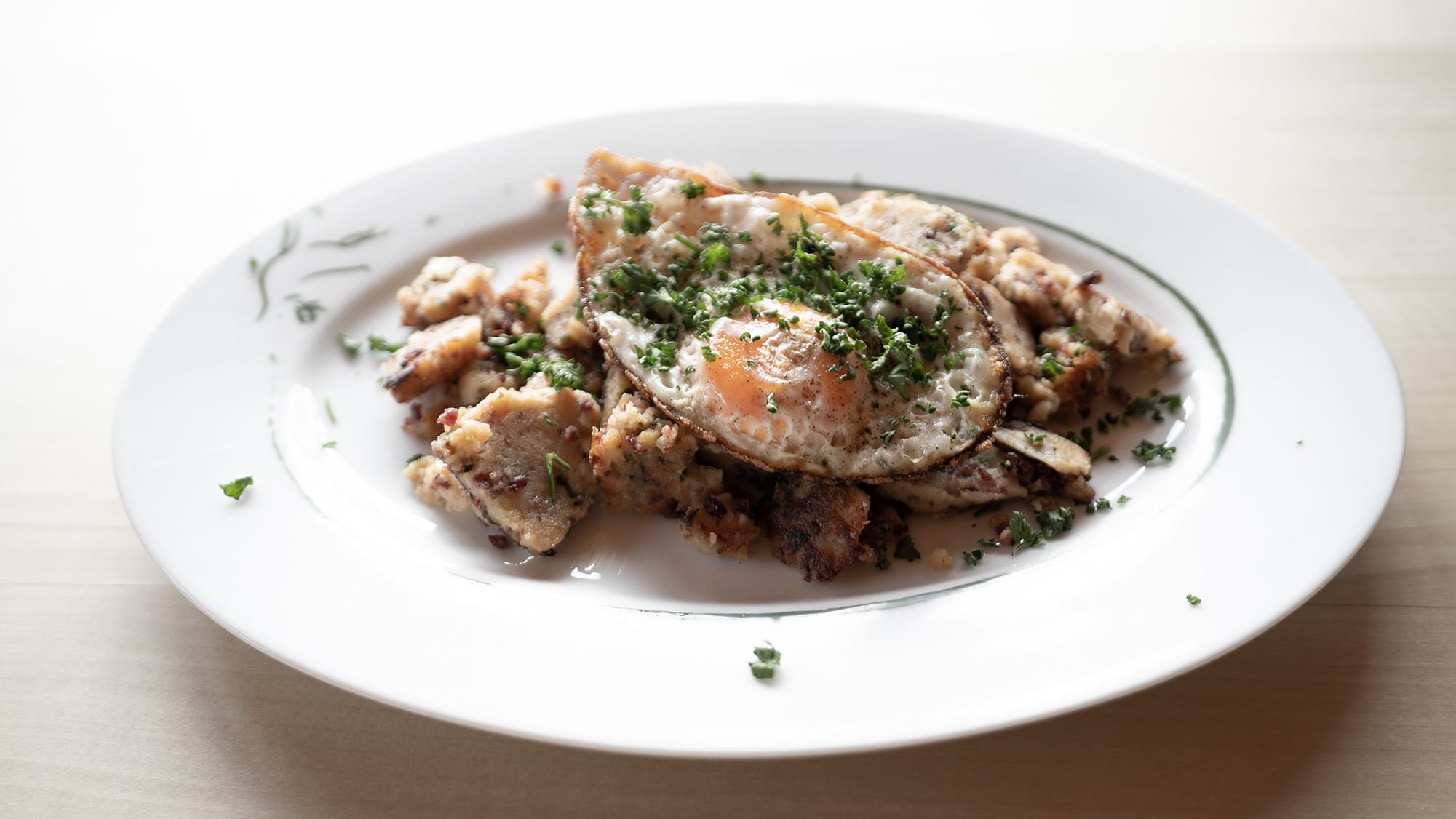 Fried potatoes with fried egg and chopped herbs on white plate