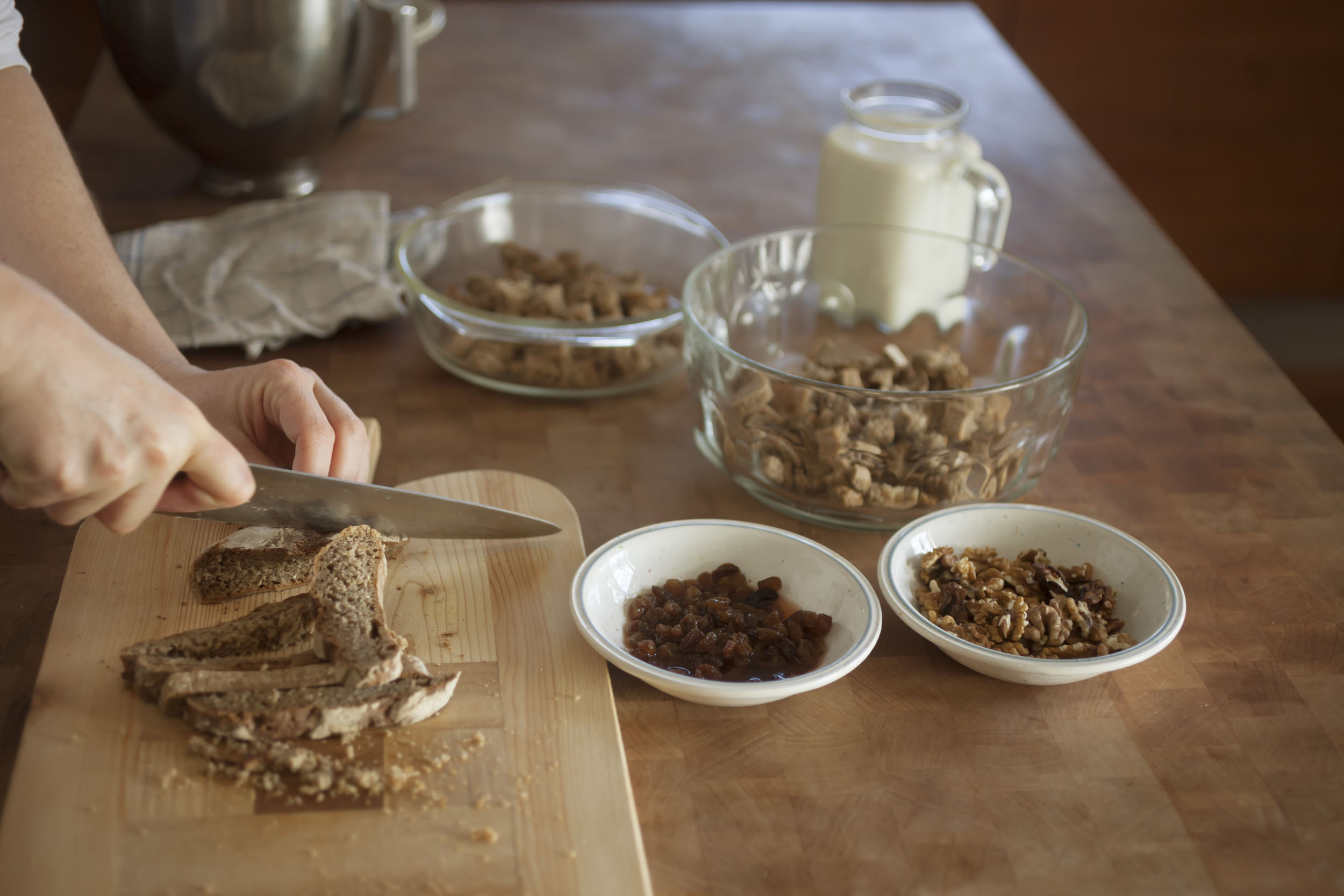 Person slicing bread on a board with bowls and milk bottle in the background