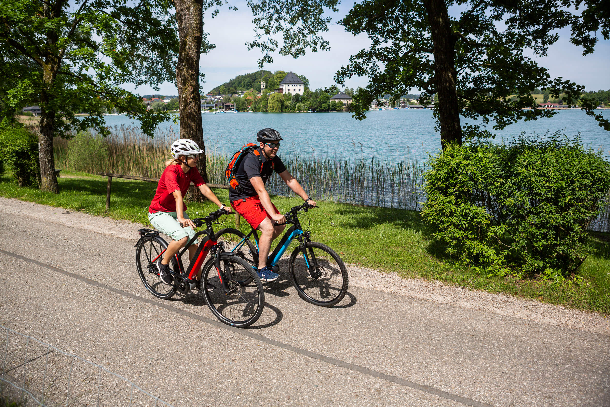 Zwei Radfahrer fahren auf einem Weg entlang eines Sees an einem sonnigen Tag