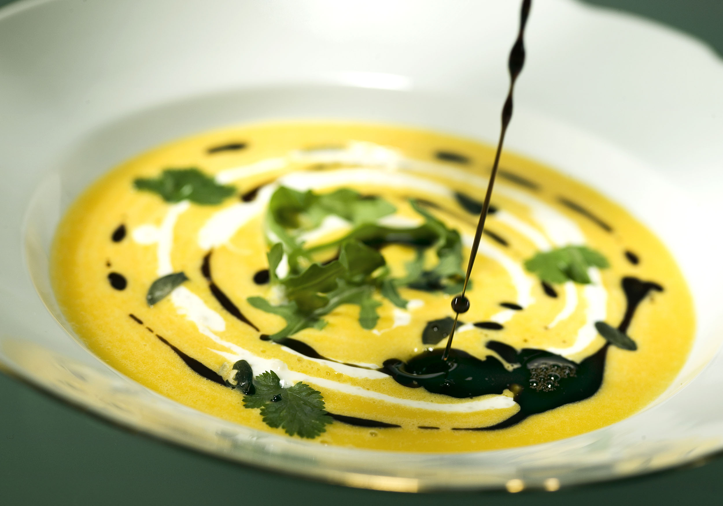 Pumpkin soup with cream, herbs, and dark oil in white bowl