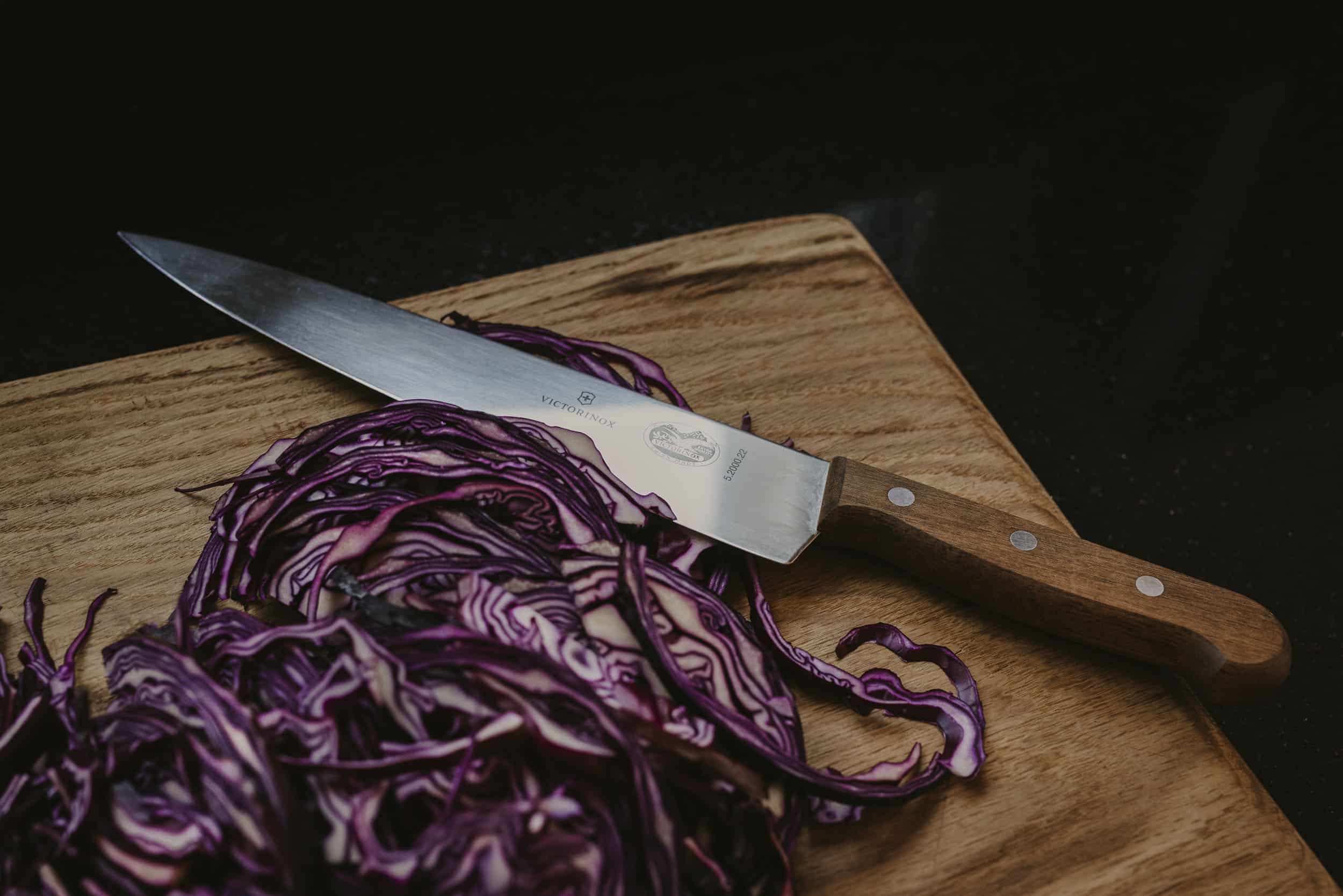 Wood-handled knife on cutting board with sliced red cabbage