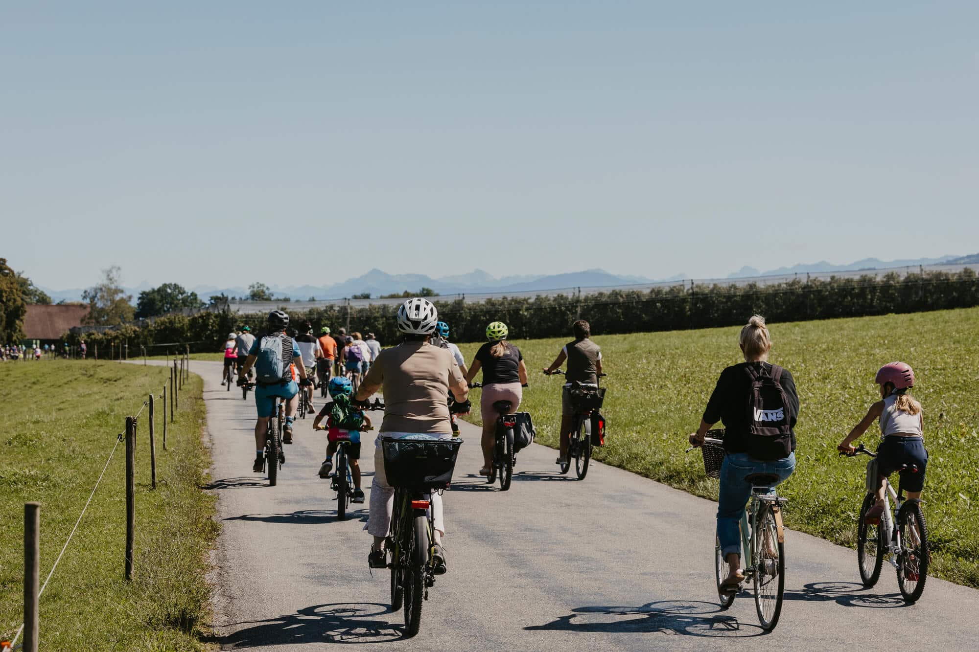 Gruppe von Menschen radelt auf Landstraße bei klarem Himmel und grüner Landschaft