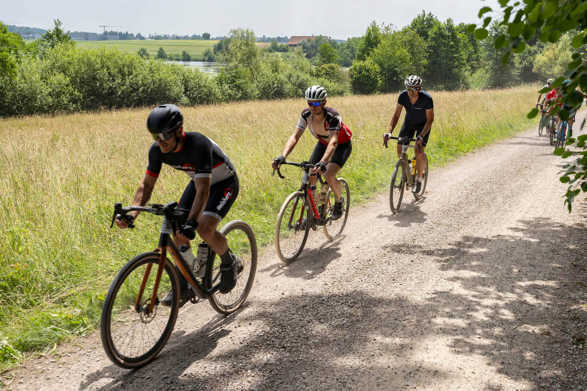 Fünf Radfahrer fahren auf einem Schotterweg in ländlicher Umgebung