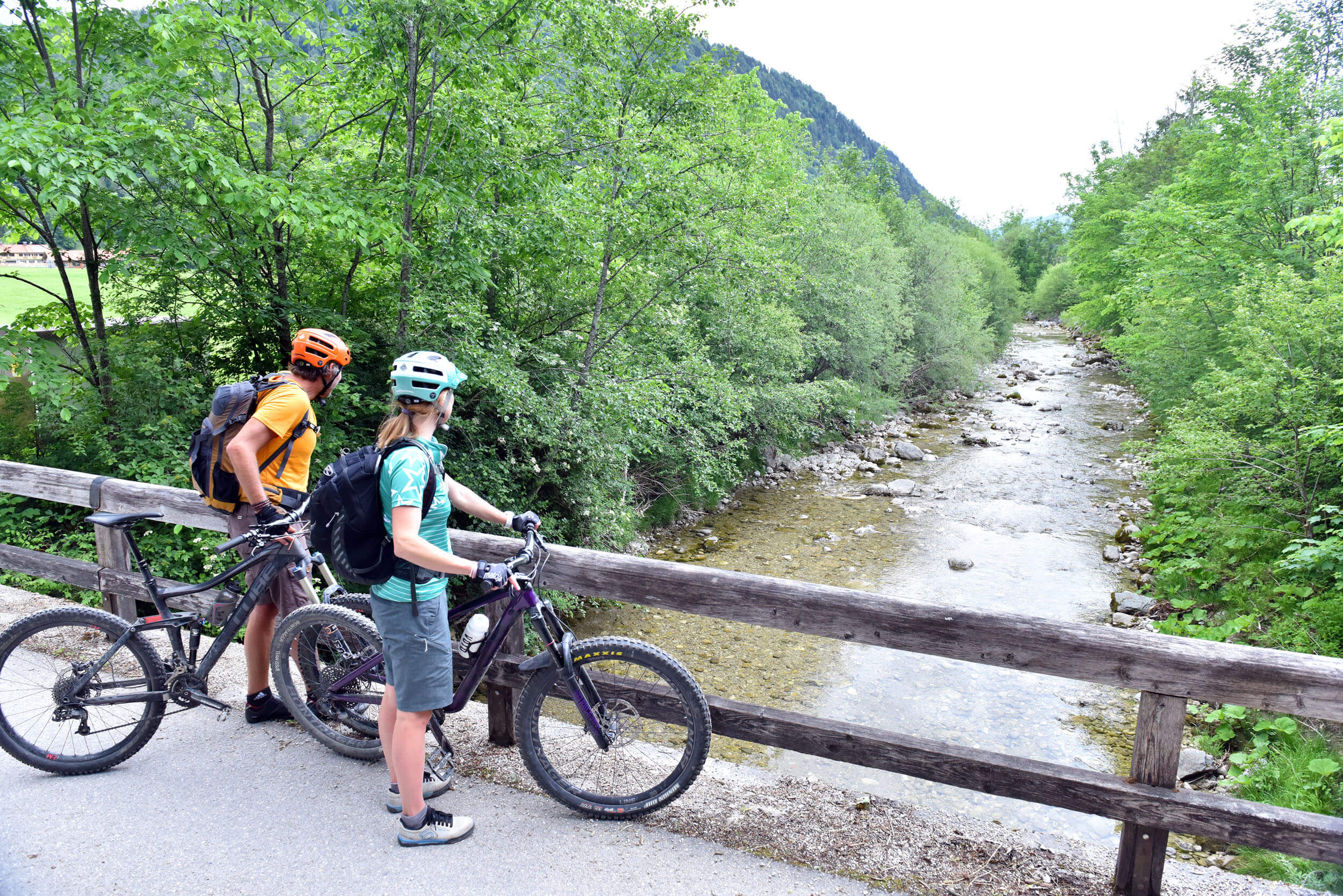 Zwei Radfahrer stehen auf einer Brücke und blicken auf einen Fluss im Wald