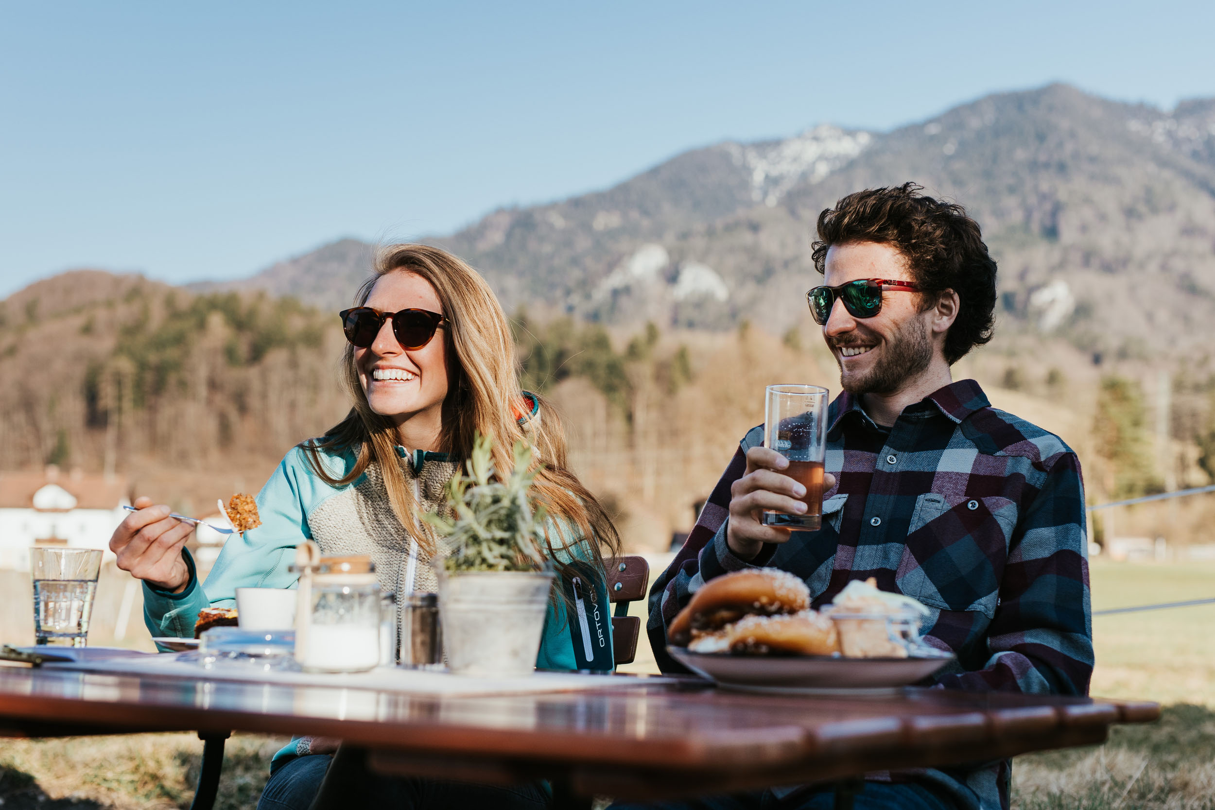 Paar genießt Mahlzeit und Getränke im Freien vor Bergkulisse