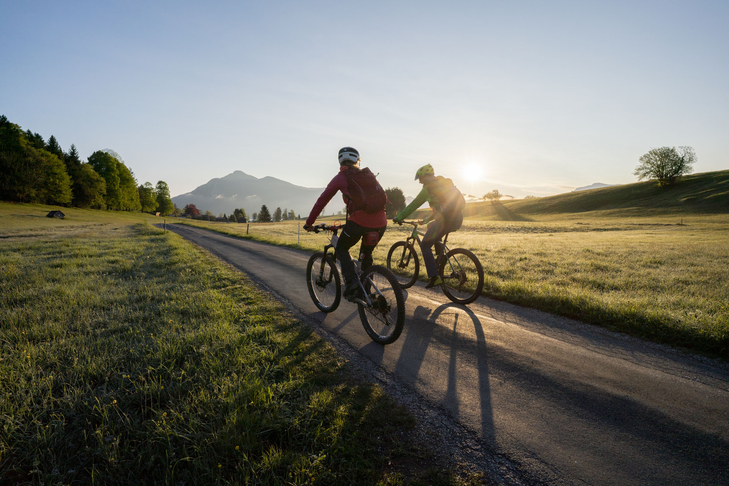 Zwei Radfahrer fahren auf Landstraße bei Sonnenaufgang