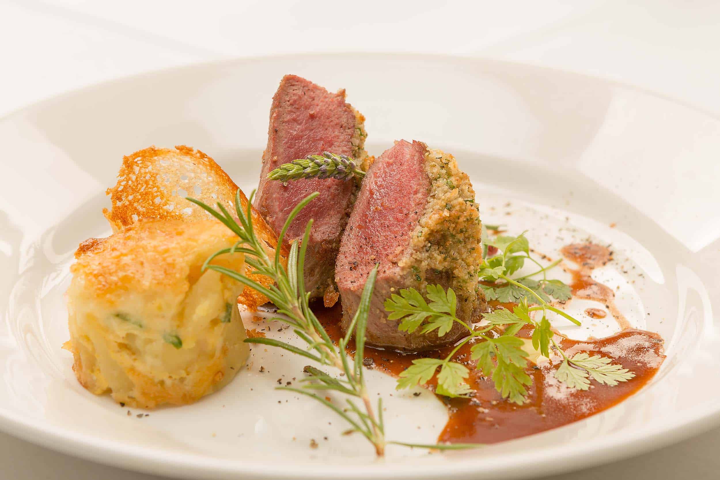 Gourmet dish with herb crust and side, garnished with fresh herbs