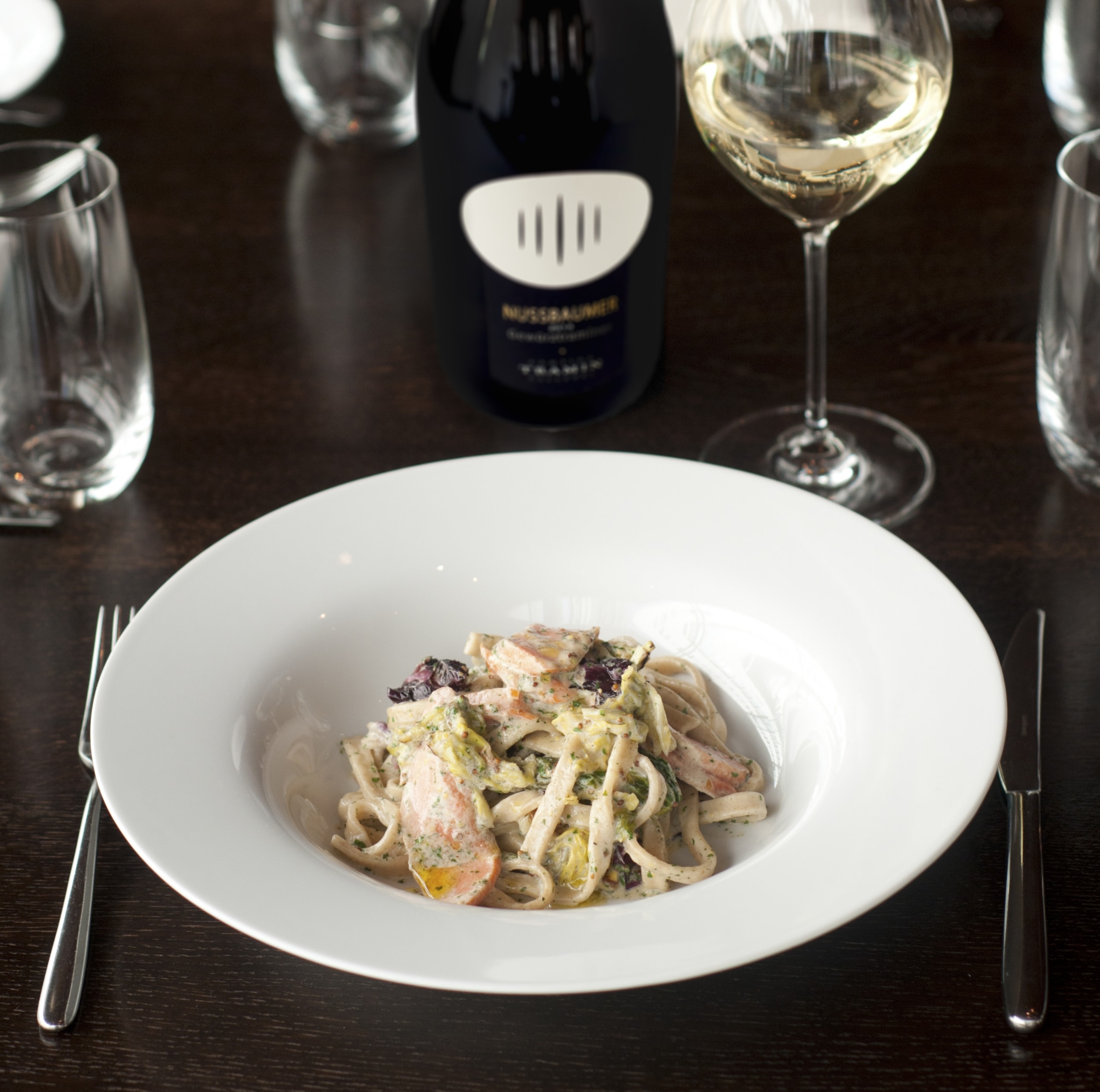 Pasta with creamy sauce served with a glass of white wine and a wine bottle