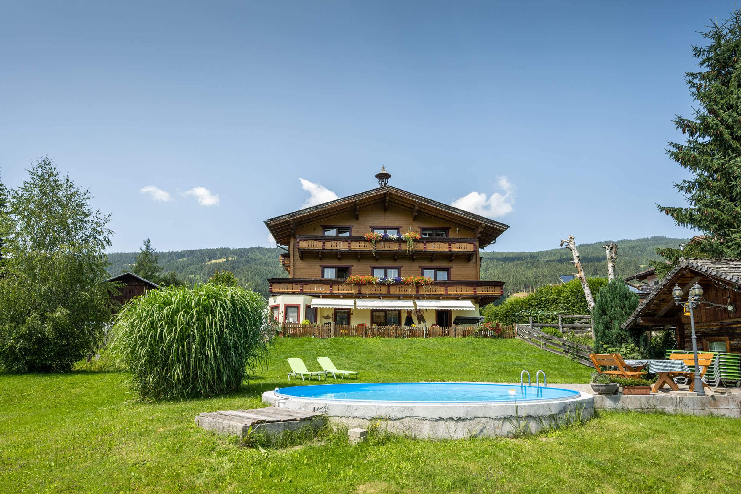 House with balcony, garden, pool and lounge chairs near forested mountain