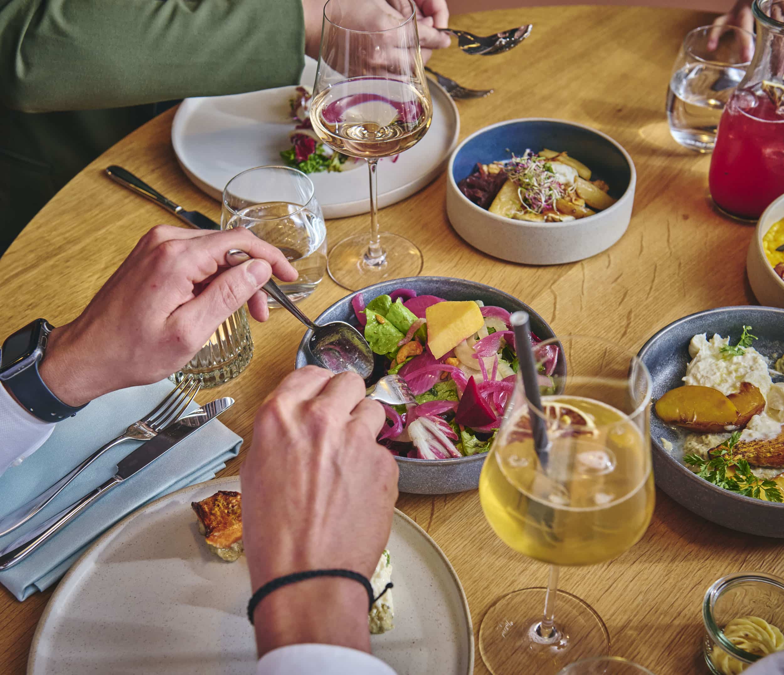 Person isst Salat und andere Speisen bei einem gedeckten Tisch mit Getränken