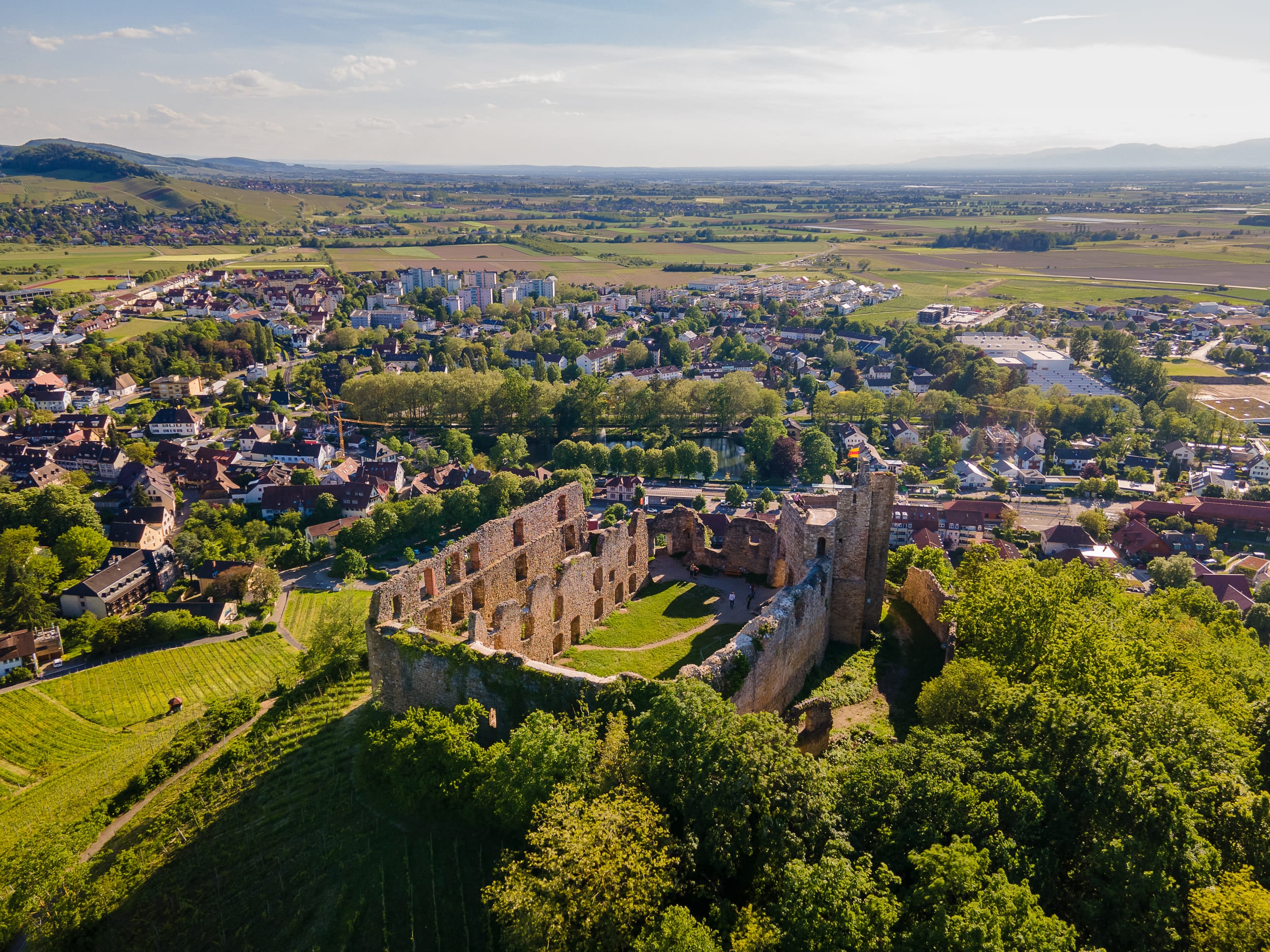 Luftaufnahme einer Burgruine über einer Stadt und grünen Feldern