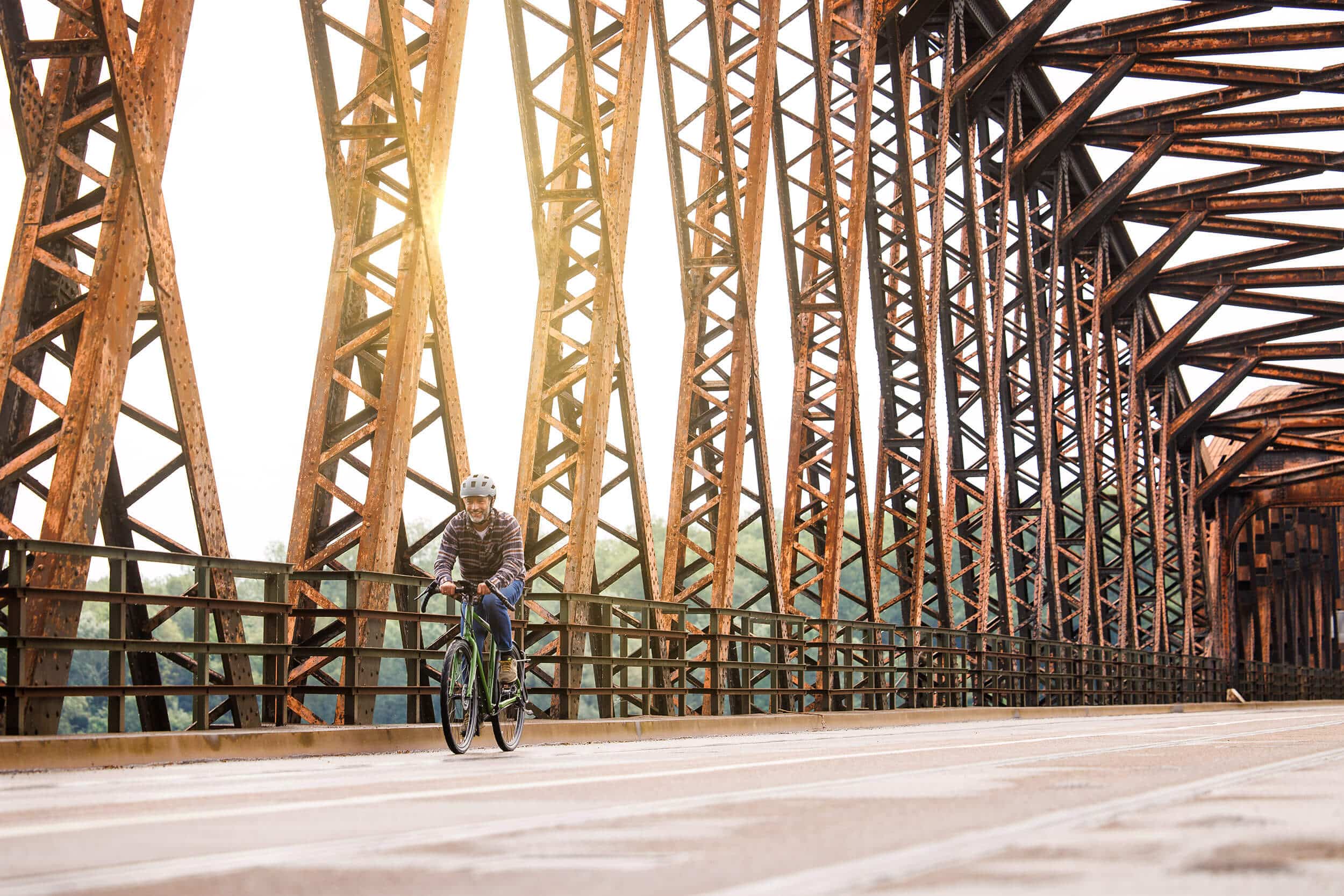 Übertreffe deine Erwartungen © Ralf Bohle GmbH Mann fährt Fahrrad auf rostiger Stahlbrücke bei Sonnenlicht