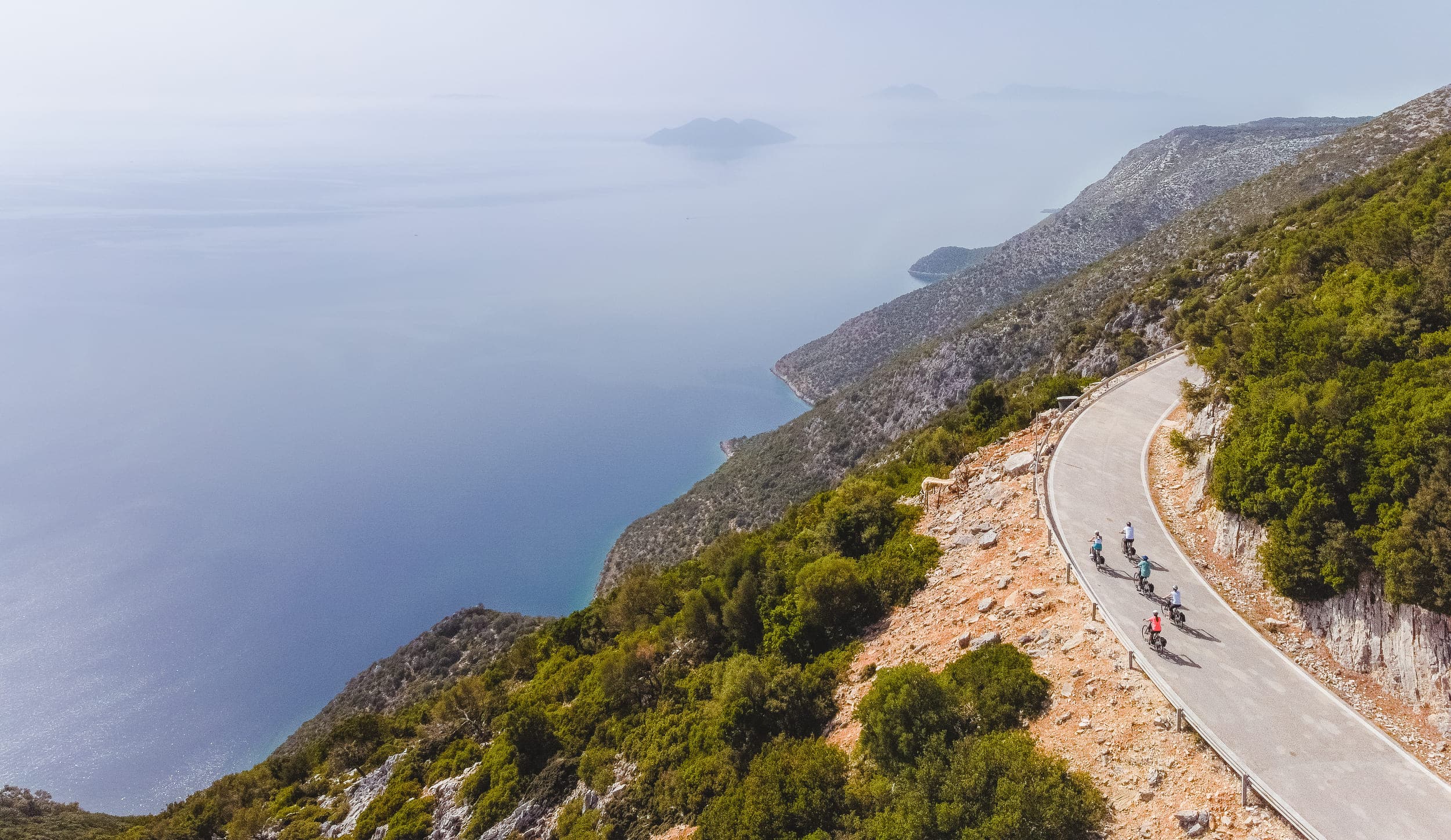 Fahrradfahrer auf einer kurvigen Bergstraße mit Meerblick