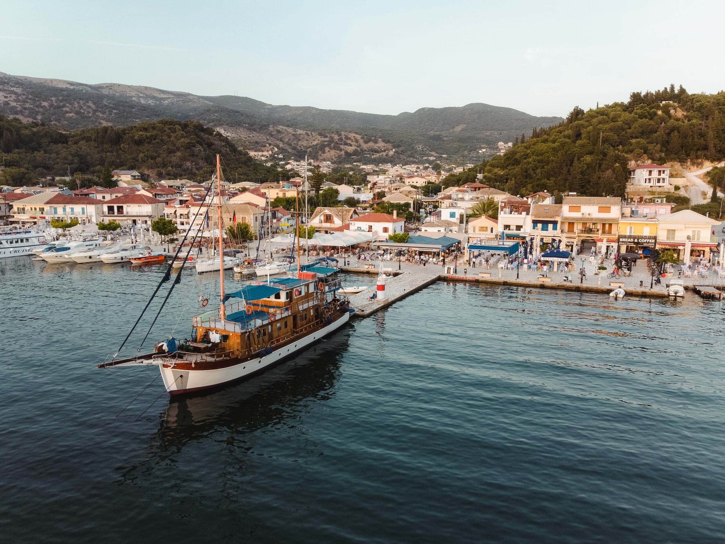 Segelboot vor einem belebten Hafen mit Bergen im Hintergrund